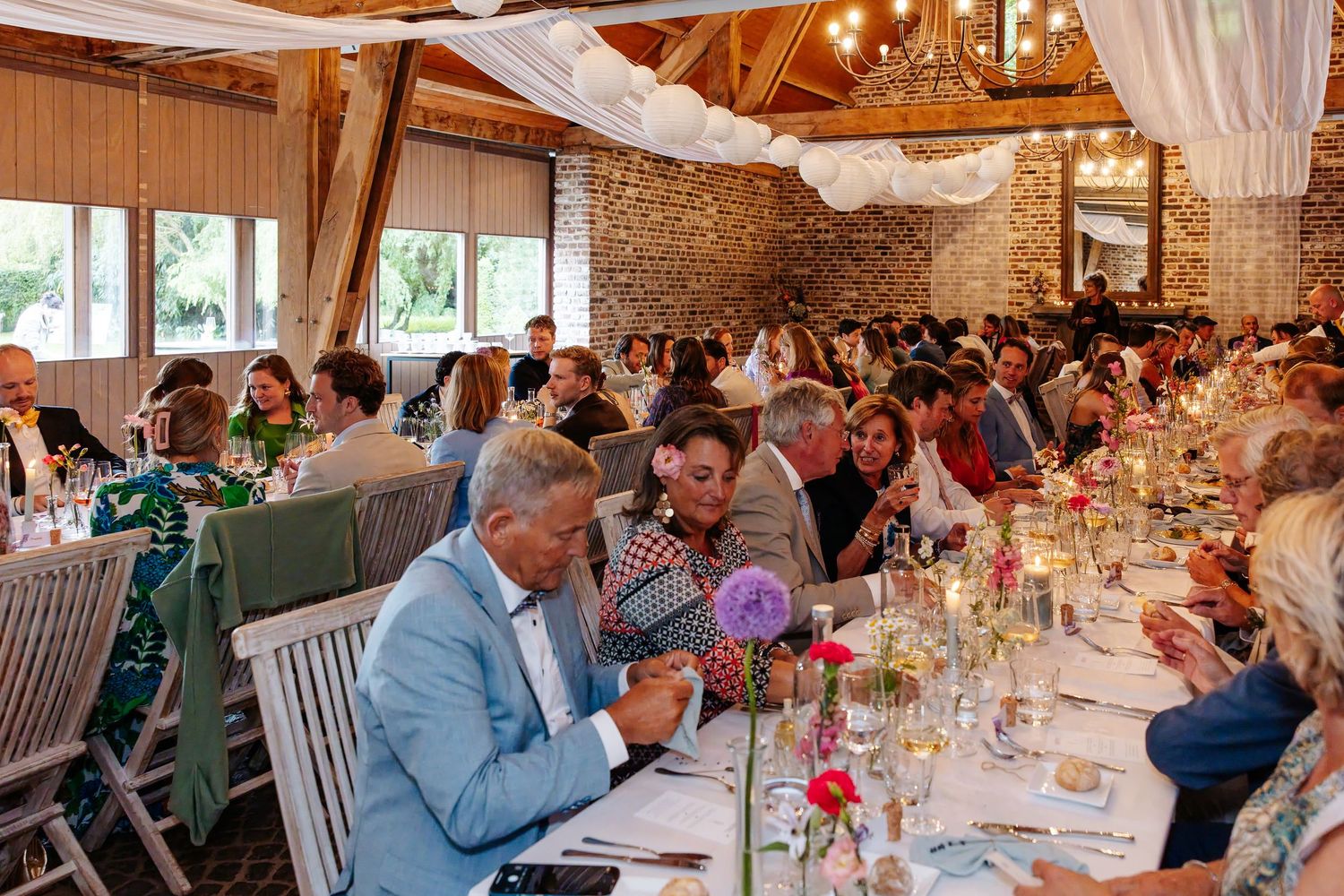 Wedding reception dinner in rustic barn venue with long decorated tables full of celebrating guests.