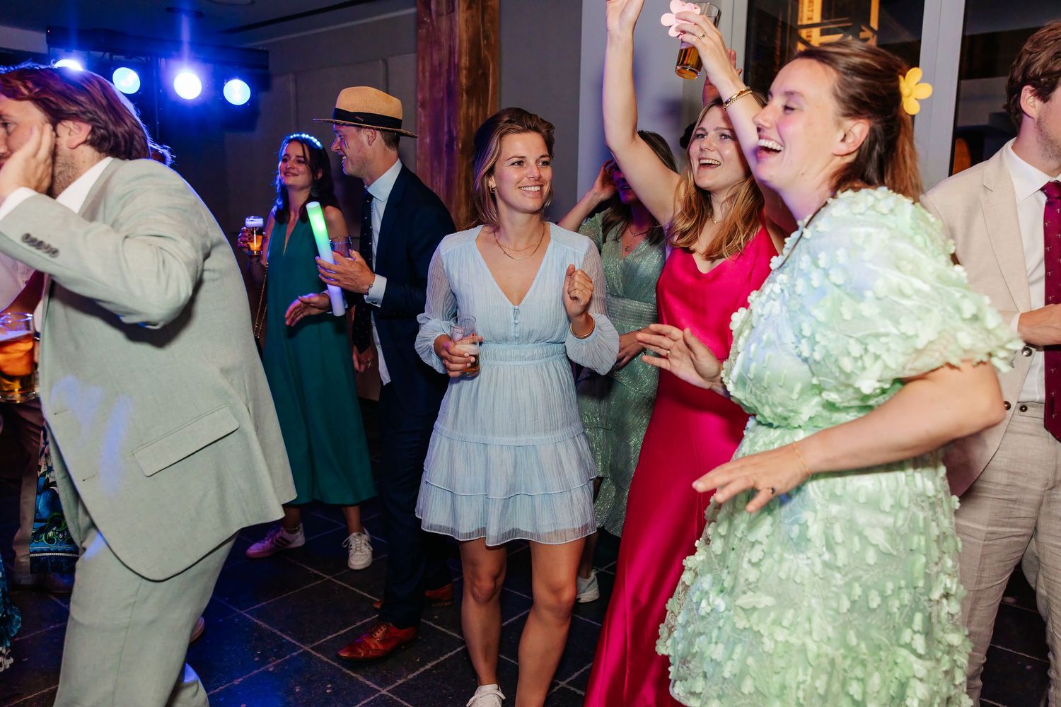 Wedding guests dancing joyfully on colorful illuminated dance floor at evening reception.
