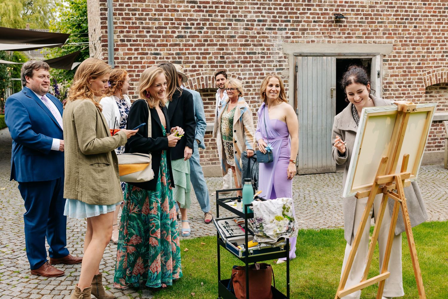 Wedding guests gathered outdoors watching a live painter create artwork at an easel.