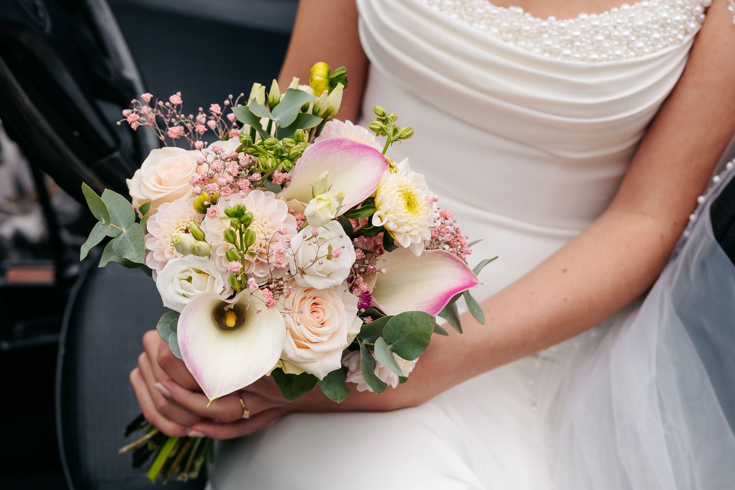 Bride in white gown holding elegant bouquet of calla lilies, roses, and pink blooms.