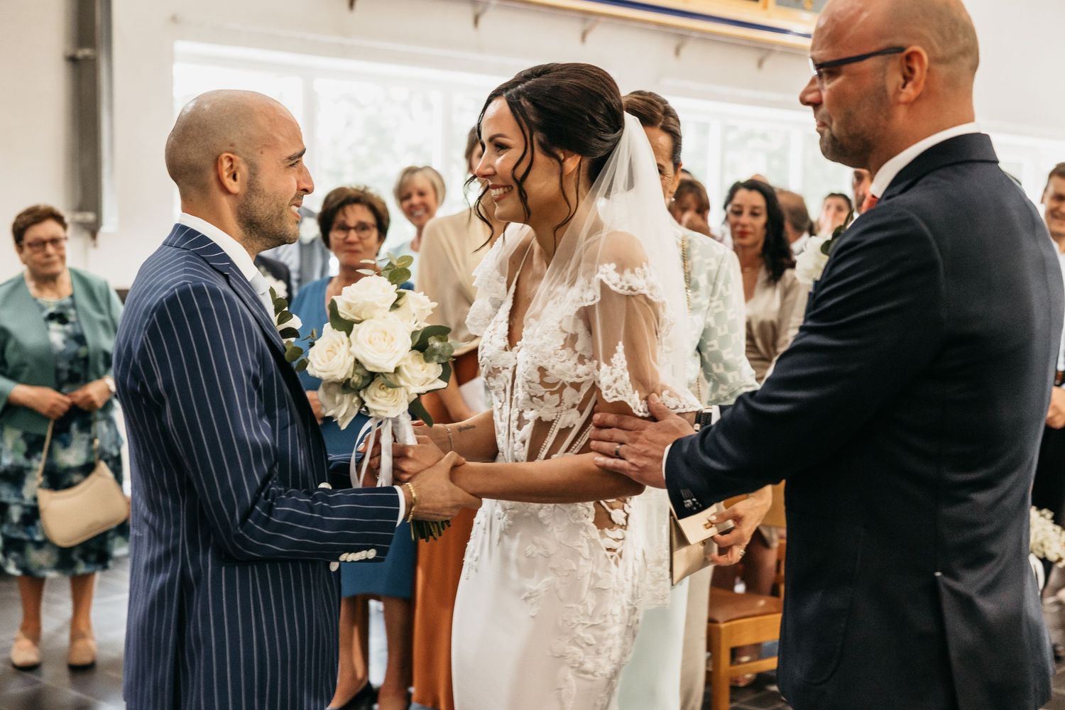 Groom in pinstripe suit holds bride's hands at church altar during wedding ceremony.