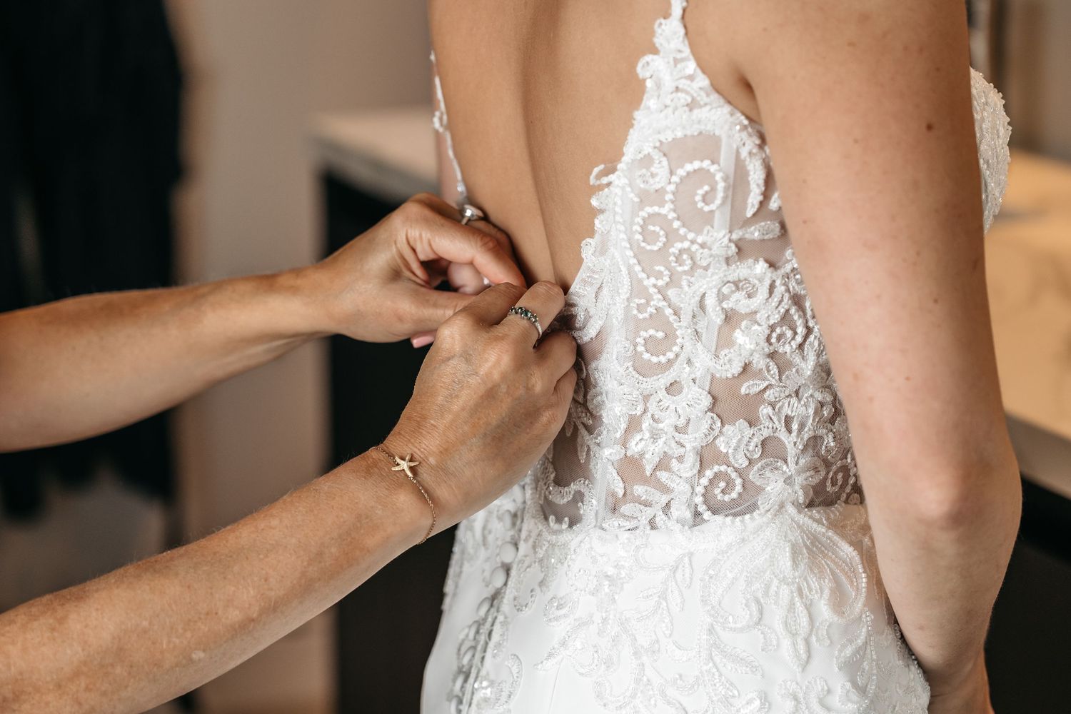 Helper carefully fastening the back buttons of a beautiful white lace wedding dress.