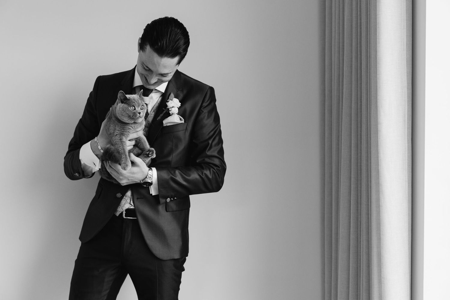 Black and white portrait of a groom in navy suit tenderly holding a gray British Shorthair cat.