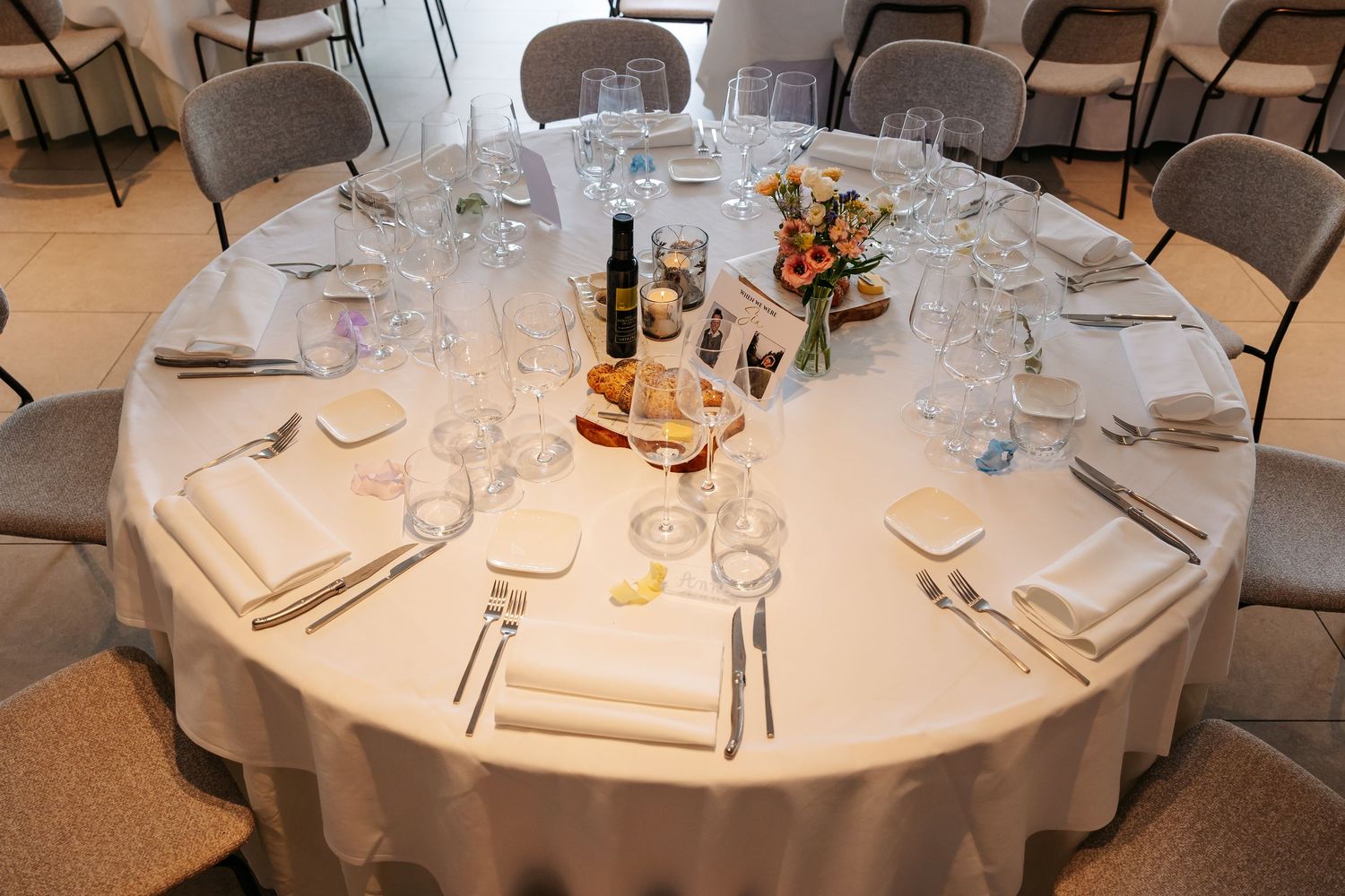 Round wedding reception table fully set with white linens, crystal glasses, napkins, and a floral centerpiece.