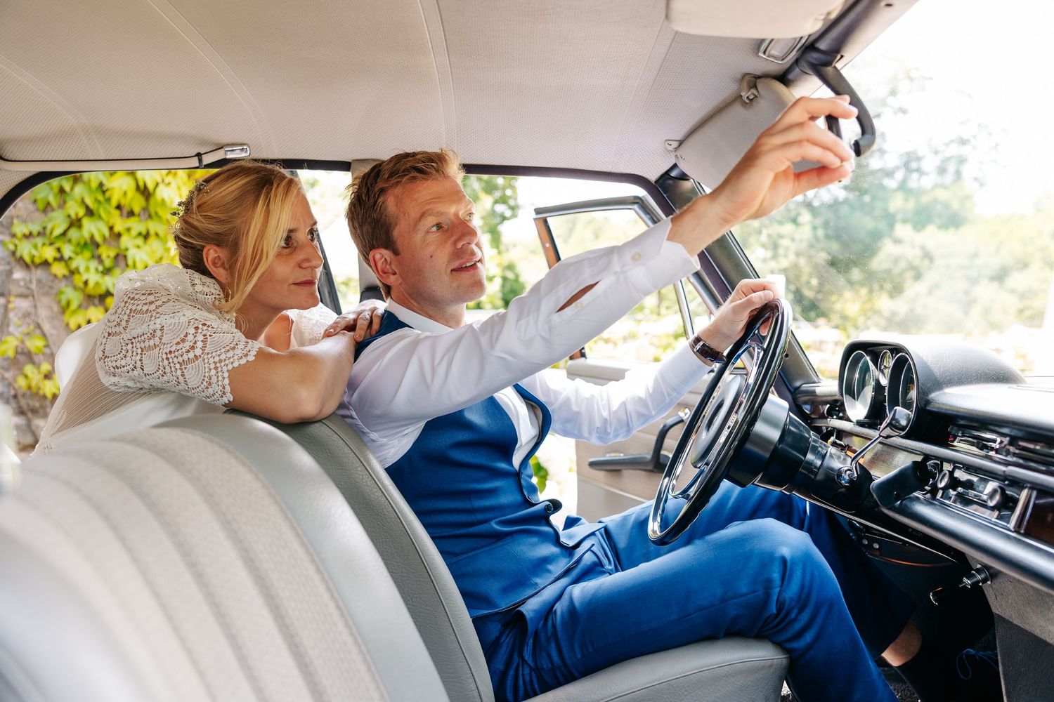 Bride and groom taking a selfie inside a vintage classic car on wedding day.