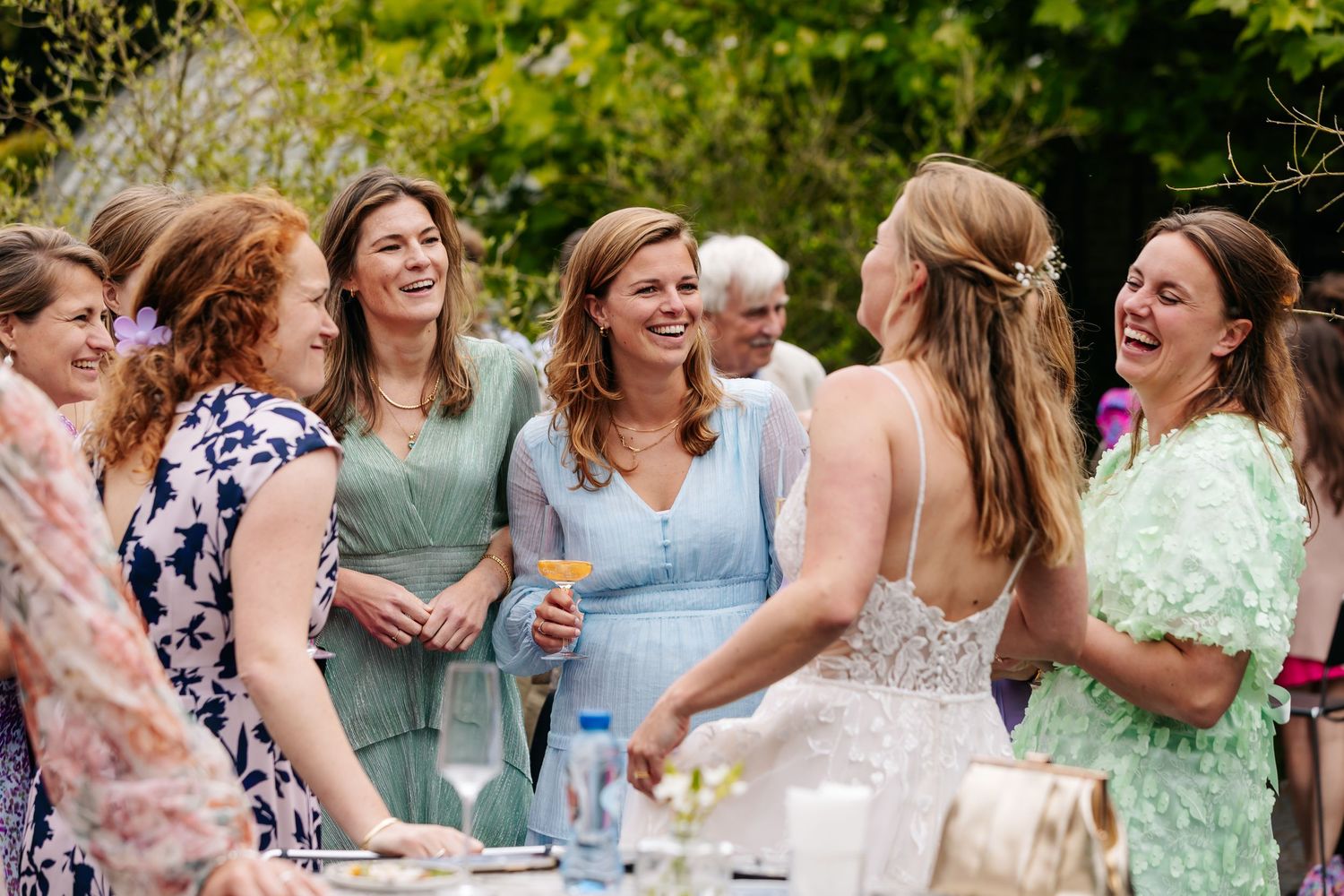 Group of smiling women in colorful dresses celebrating with bride at outdoor wedding.