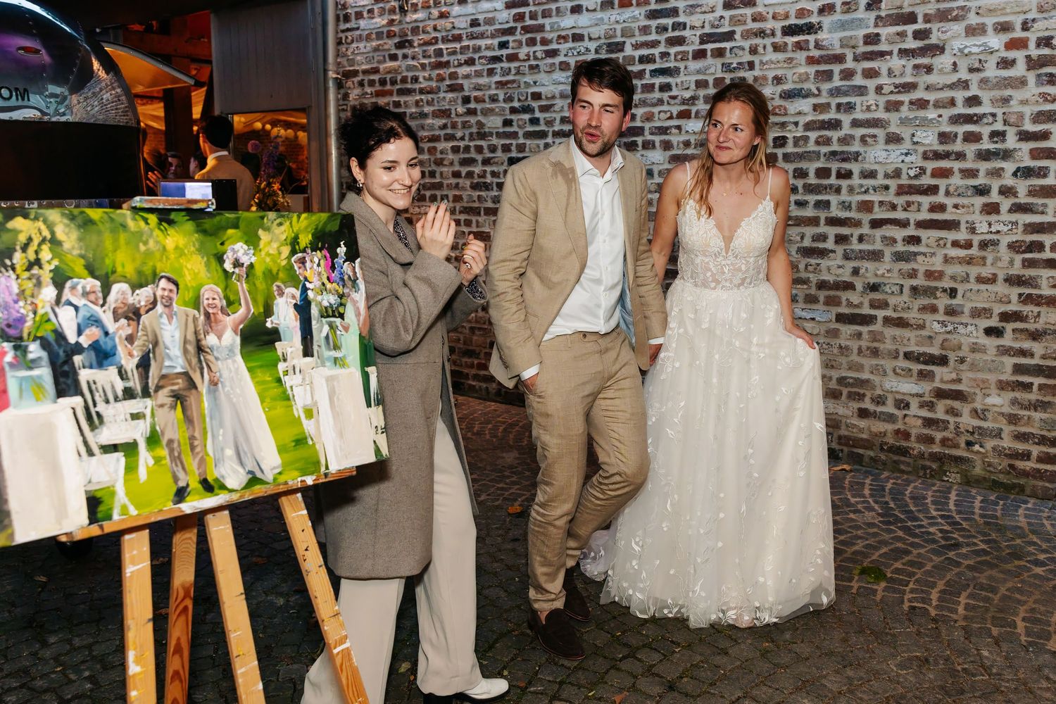 Bride and groom admiring live wedding painting with artist at reception venue.