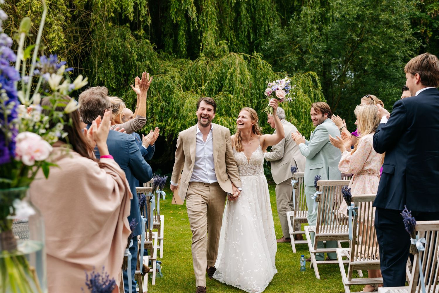 Newlyweds walk joyfully down the aisle as guests cheer and wave in celebration.