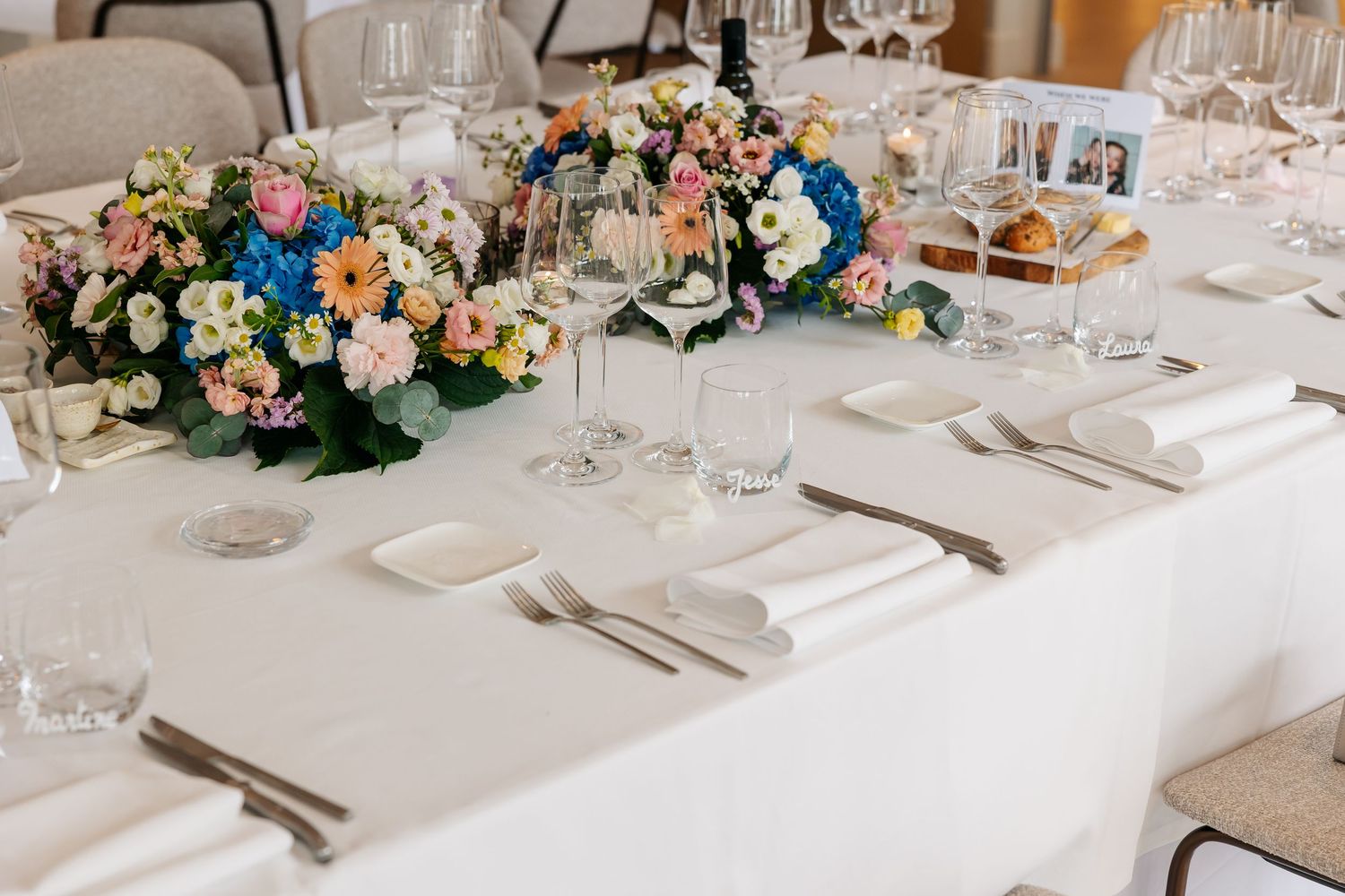 Elegant wedding reception long table with colorful floral centerpieces, crystal glasses, and white linens.