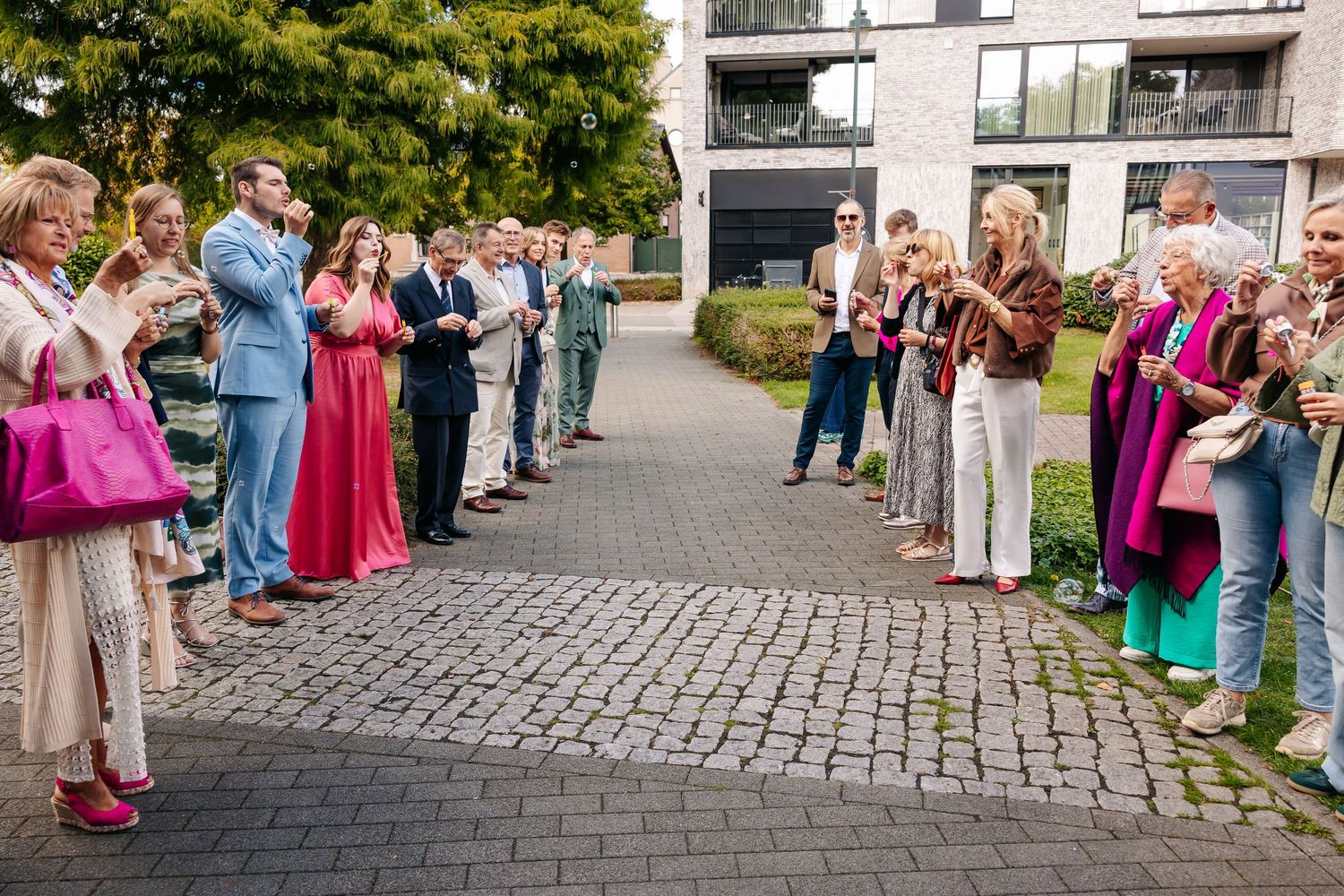 Wedding guests lining a cobblestone path forming a guard of honor outside modern building.