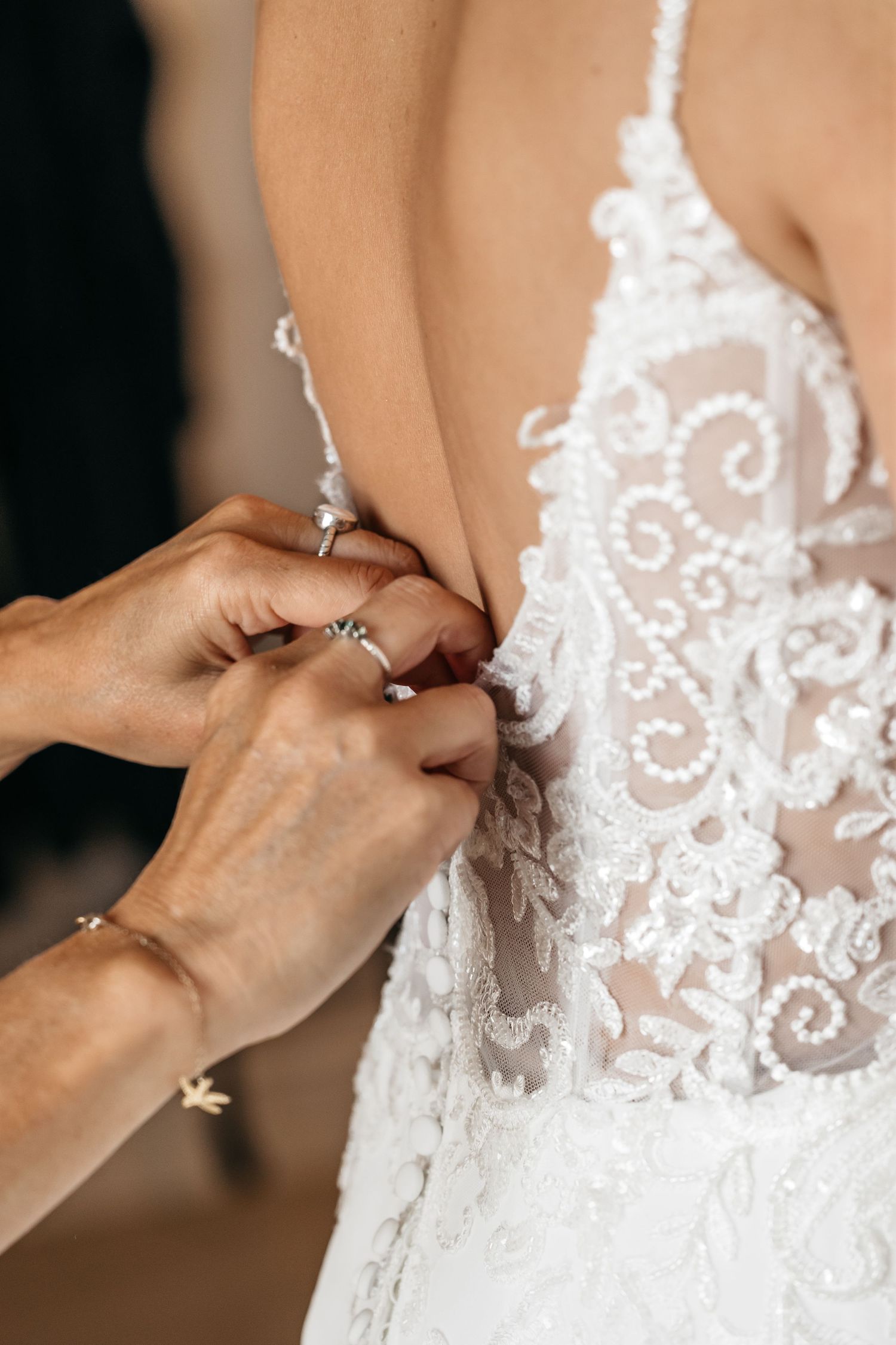Close-up of hands buttoning delicate pearl buttons on intricate white lace bridal gown.