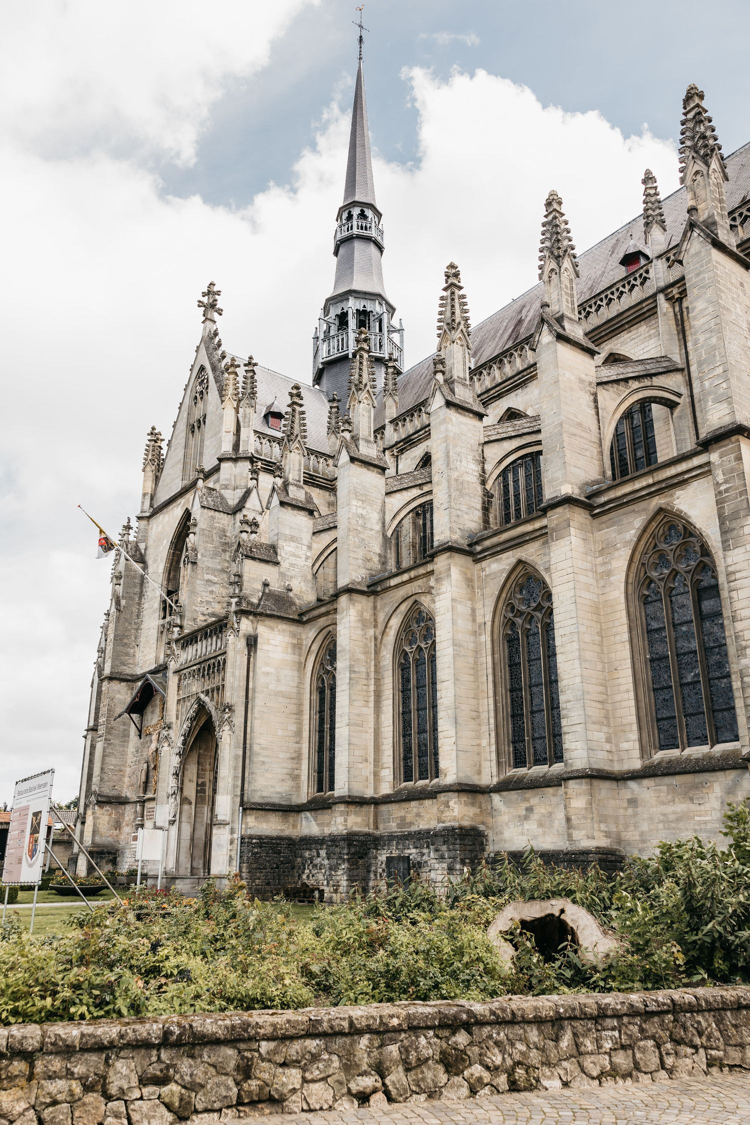 Gothic cathedral exterior with pointed spire and ornate stone architecture under cloudy sky.