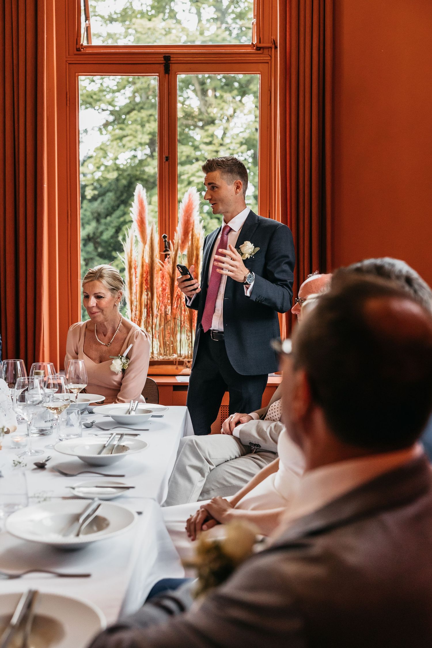 Groom delivers wedding speech holding bottle at elegant reception dinner table.