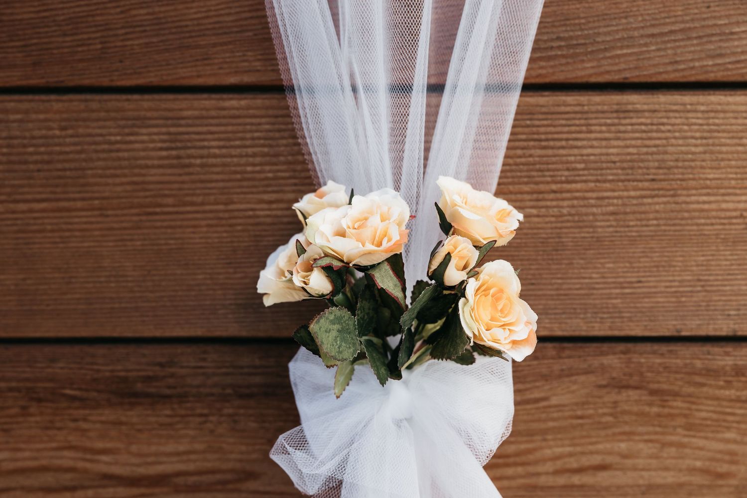 Elegant wedding decoration featuring cream roses and white tulle bow on rustic wooden background.