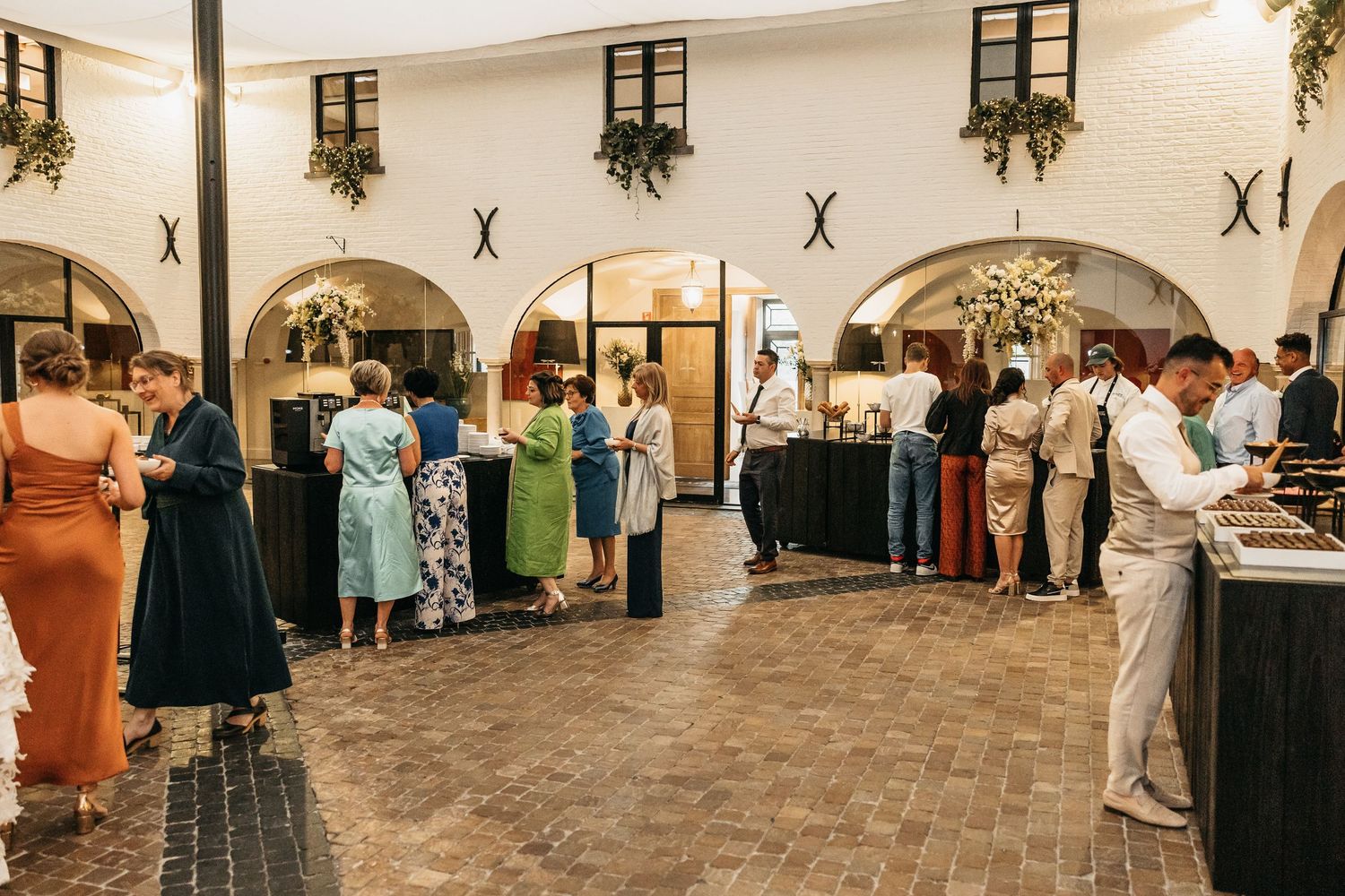 Wedding reception guests mingling in a elegant venue with arched doorways and lush floral decorations.