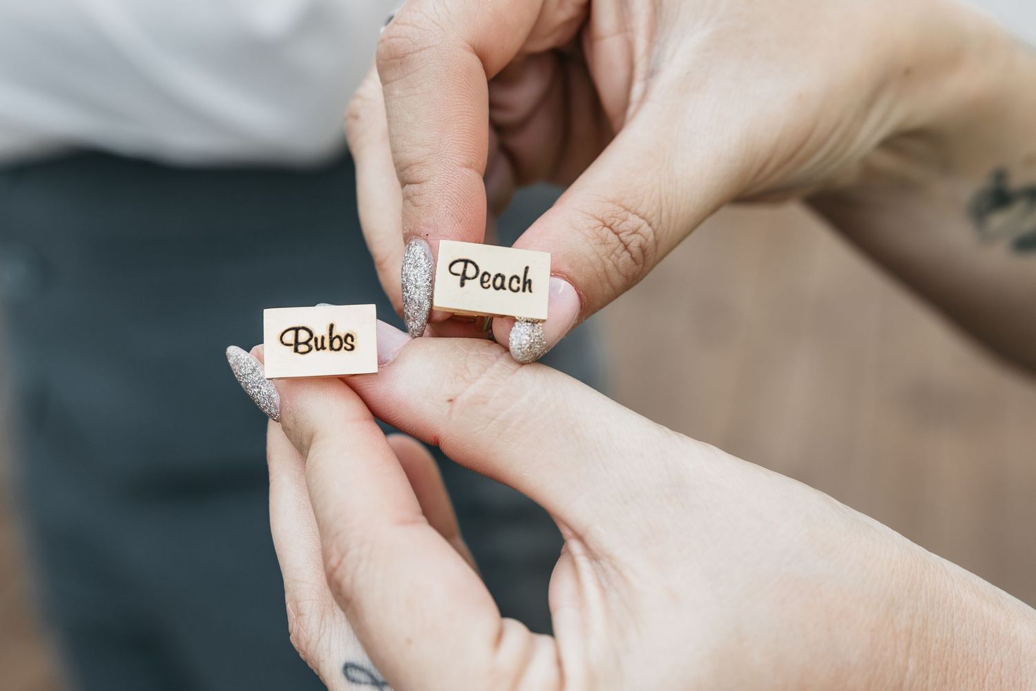 Close-up of hands holding two small wooden tiles engraved with the nicknames Bubs and Peach.