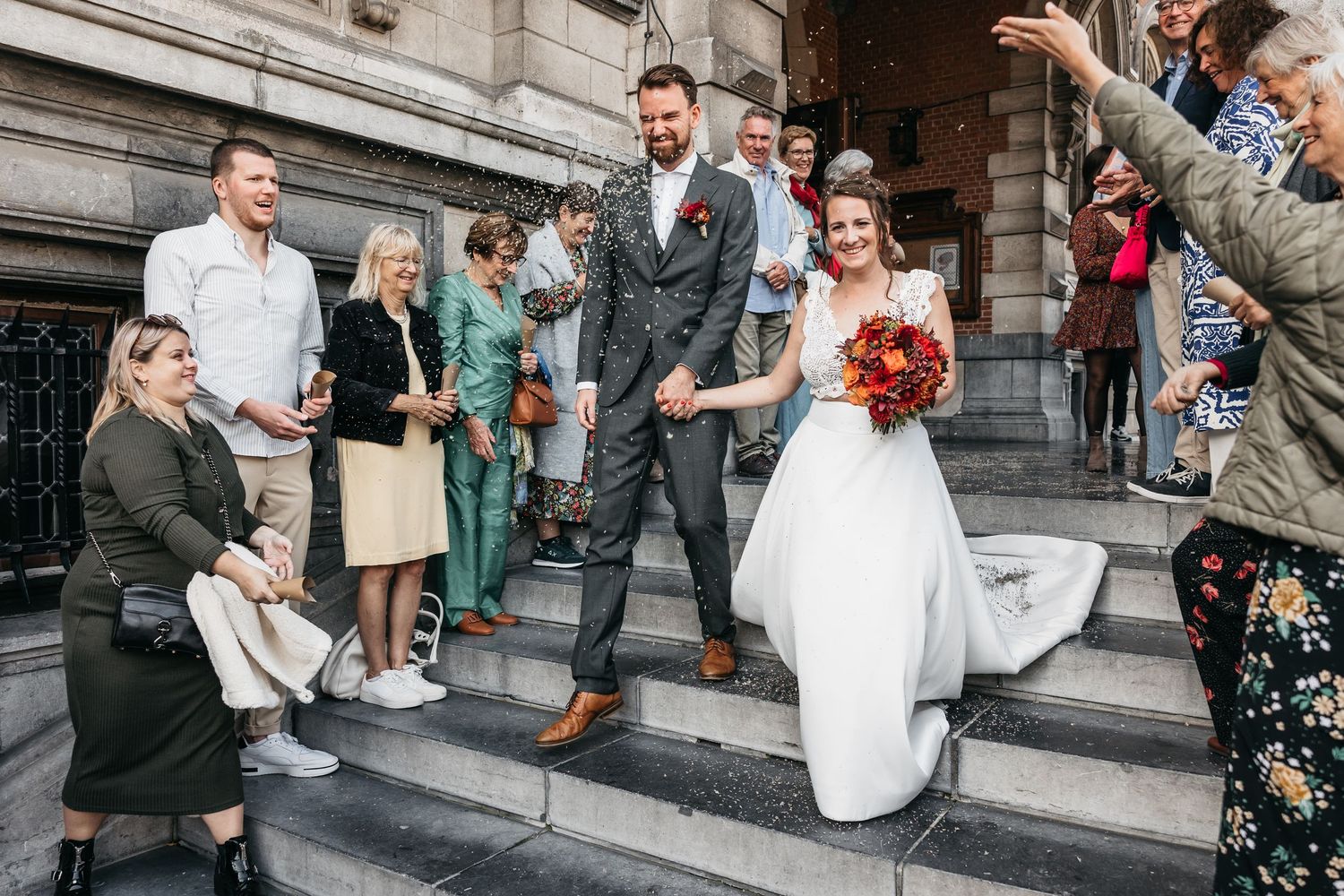 Bride and groom walk down historic stone steps surrounded by cheering wedding guests outdoors.