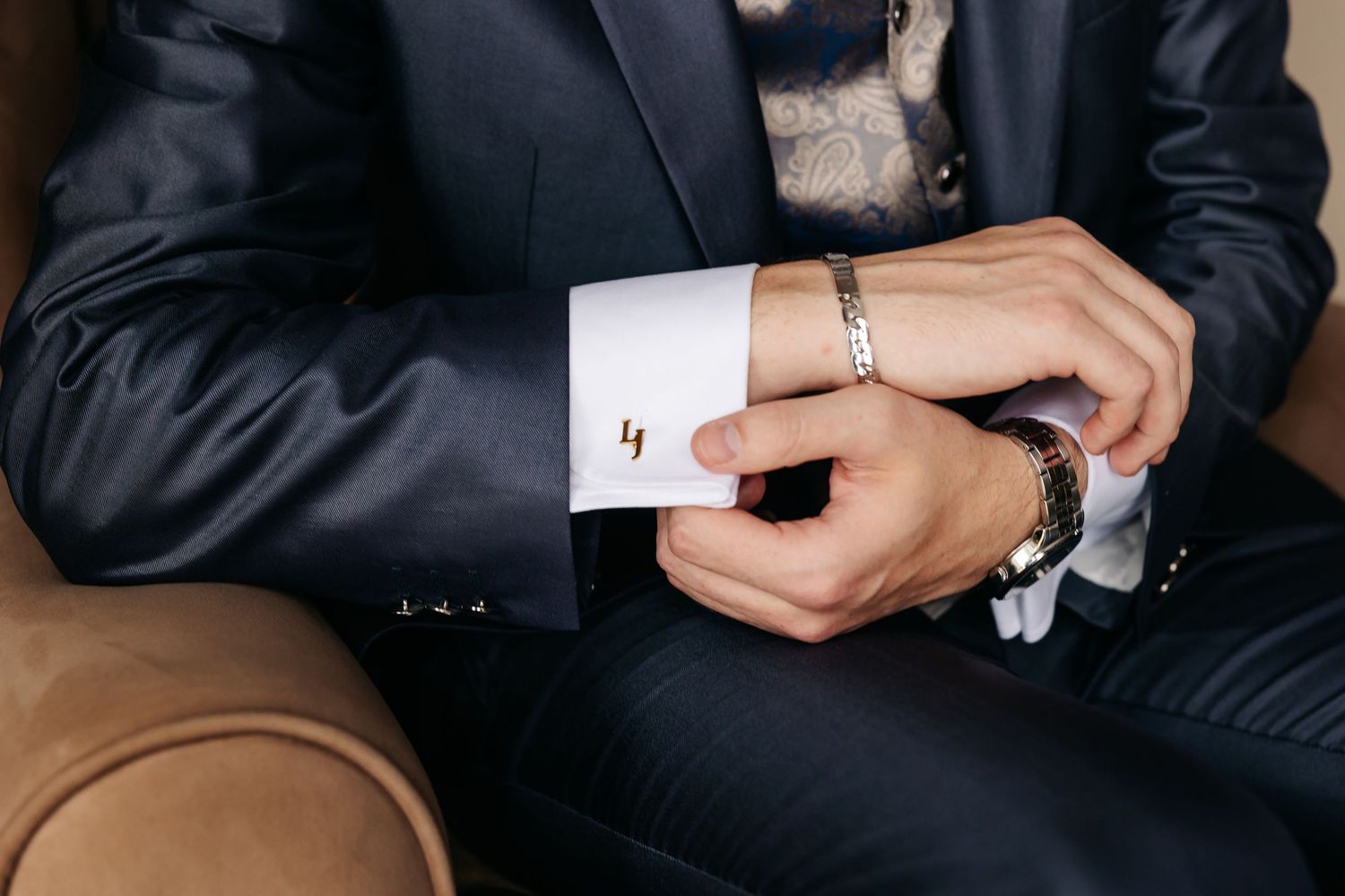 Close-up of groom adjusting gold cufflinks on white dress shirt sleeve before wedding.