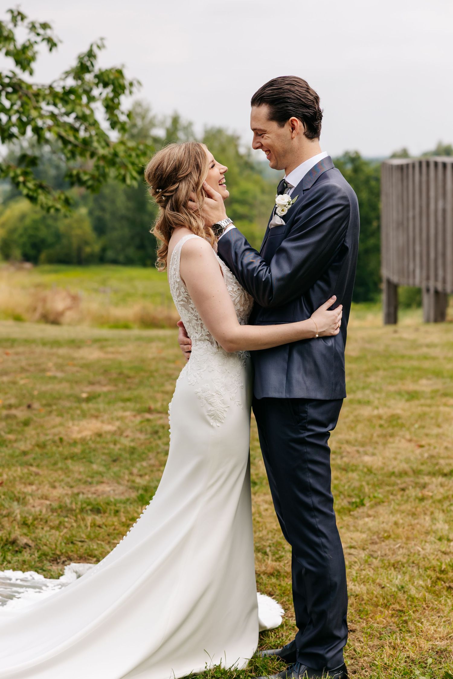 Bride and groom embracing and smiling at each other while standing in a green field on their wedding day.
