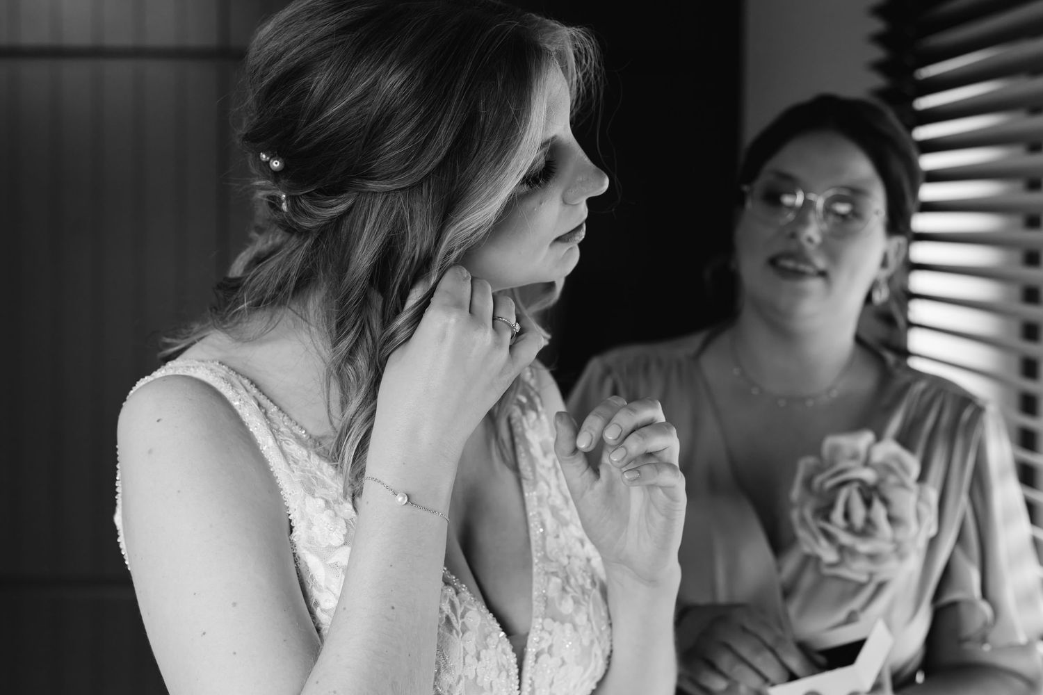 Black and white photo of bride in lace gown touching her face with bridesmaid watching during bridal prep.