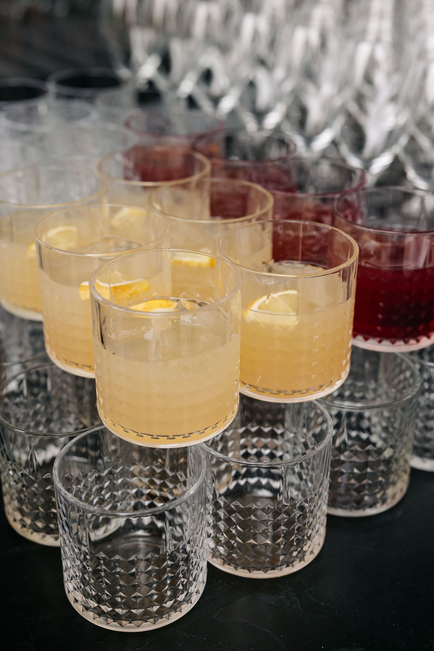 Elegant crystal glasses filled with yellow lemon and red berry cocktails arranged on dark surface.