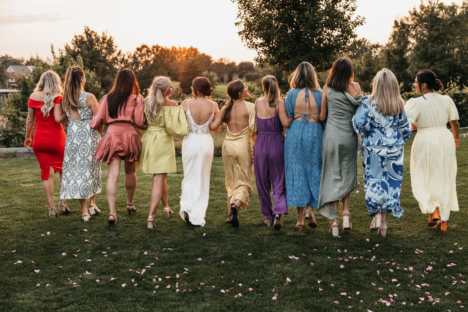 Bride and female wedding guests walking away in colorful dresses at sunset outdoor wedding.