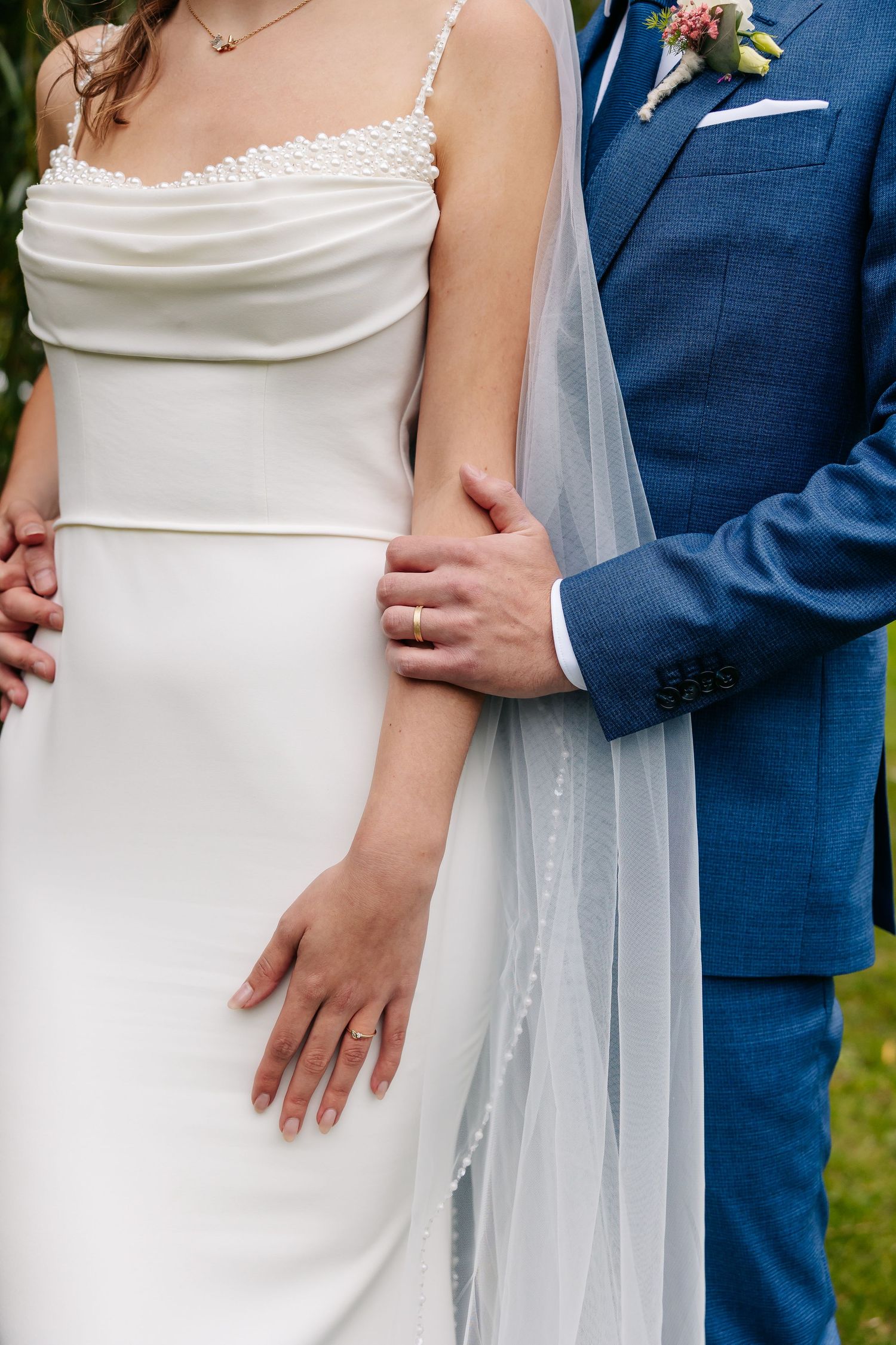 Close-up of bride in white spaghetti-strap gown and groom in blue suit holding each other.