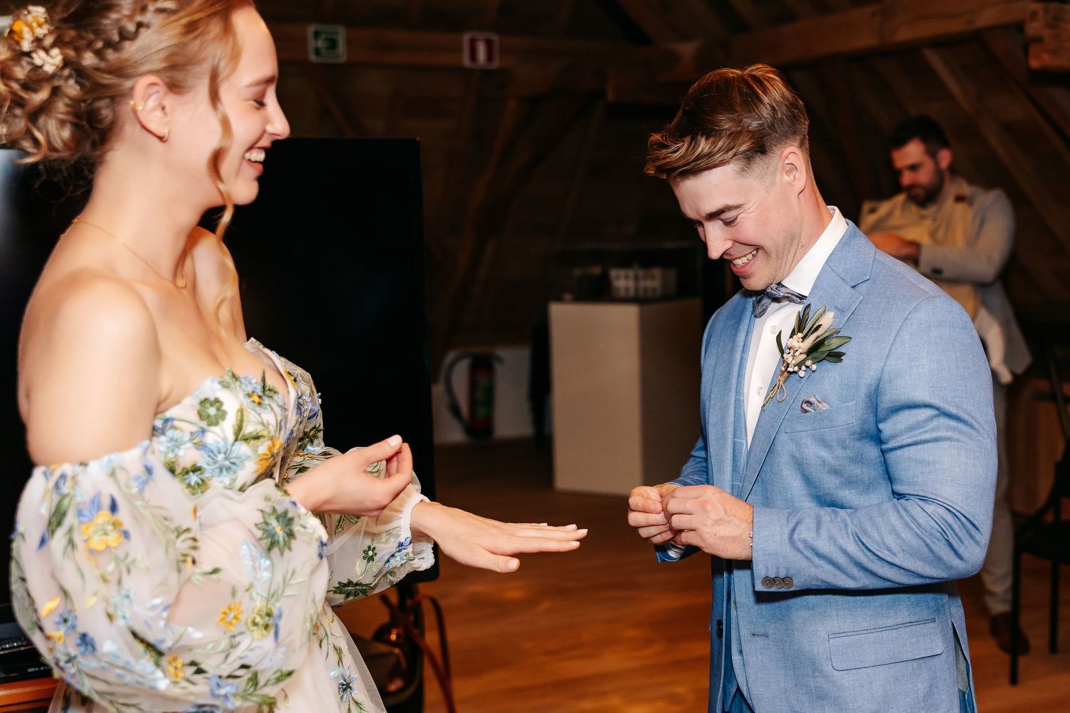 Laughing bride and groom share joyful moment during wedding ring exchange at indoor ceremony.