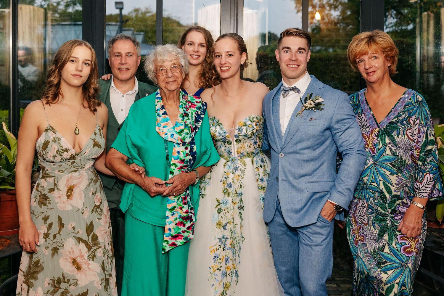 Wedding couple posing with family members including elderly grandmother in colorful outfits at reception venue.