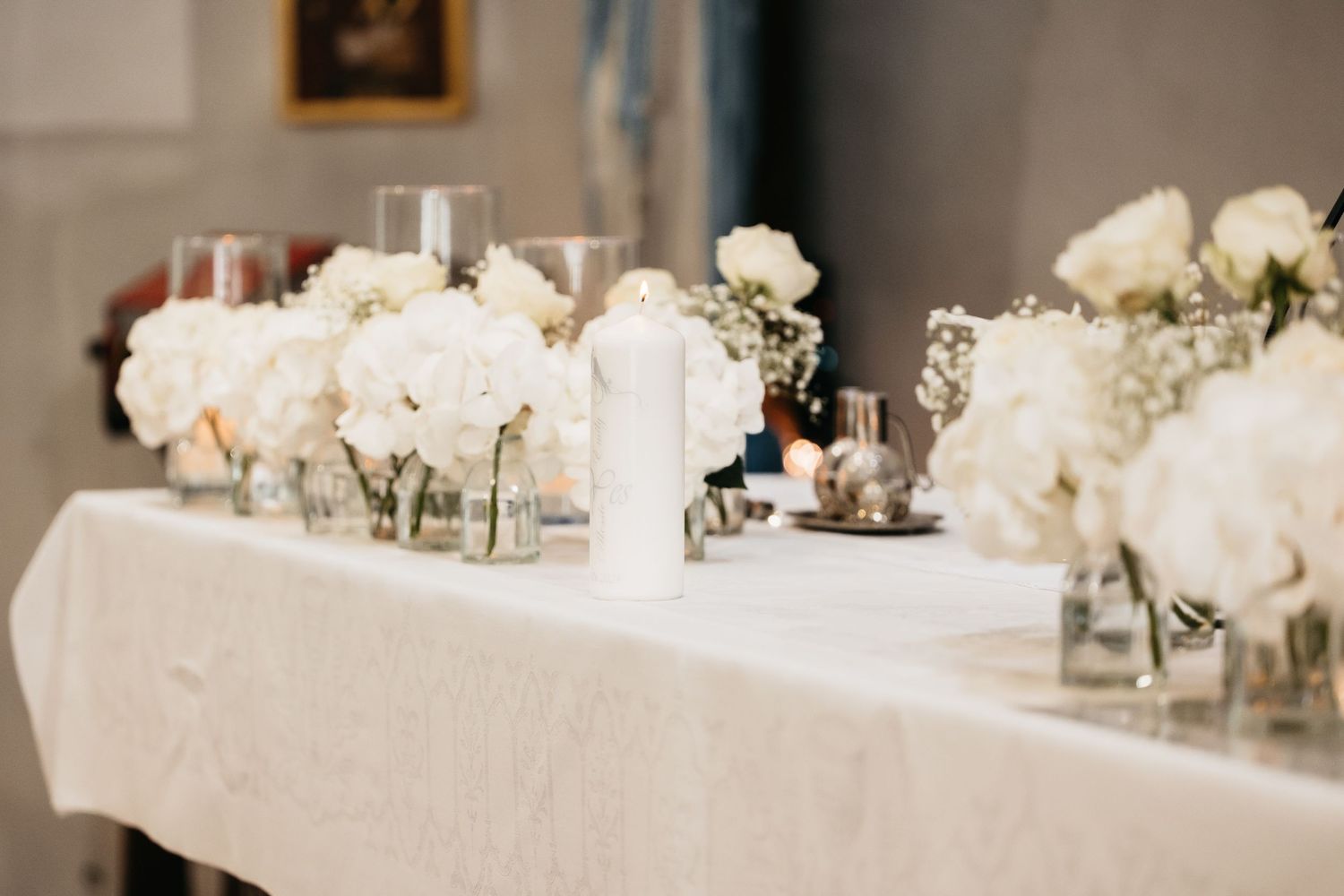 Elegant wedding altar table decorated with white hydrangeas, roses, candles, and glassware.