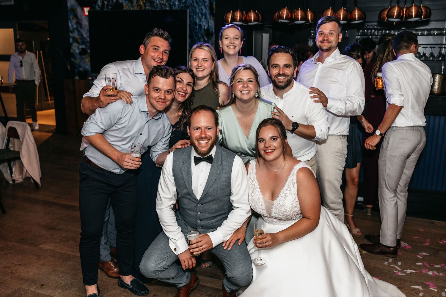 Bride and groom pose for a fun group photo with smiling friends and family at their wedding reception.