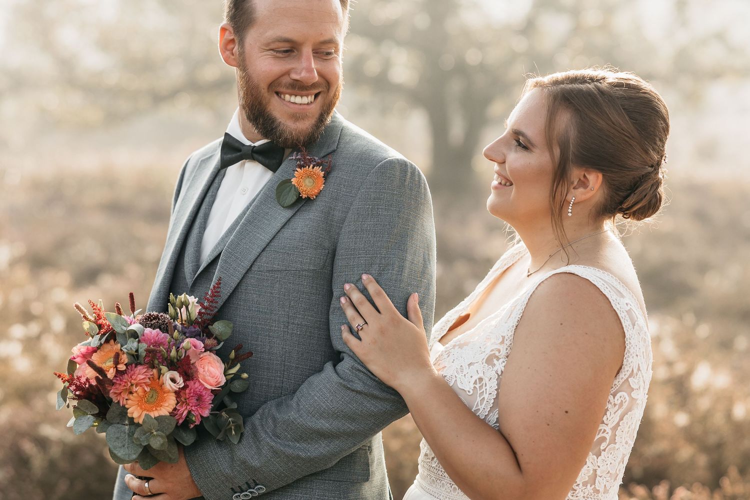 Happy bride touches grooms chest as they share a joyful laugh during their outdoor autumn wedding portraits.