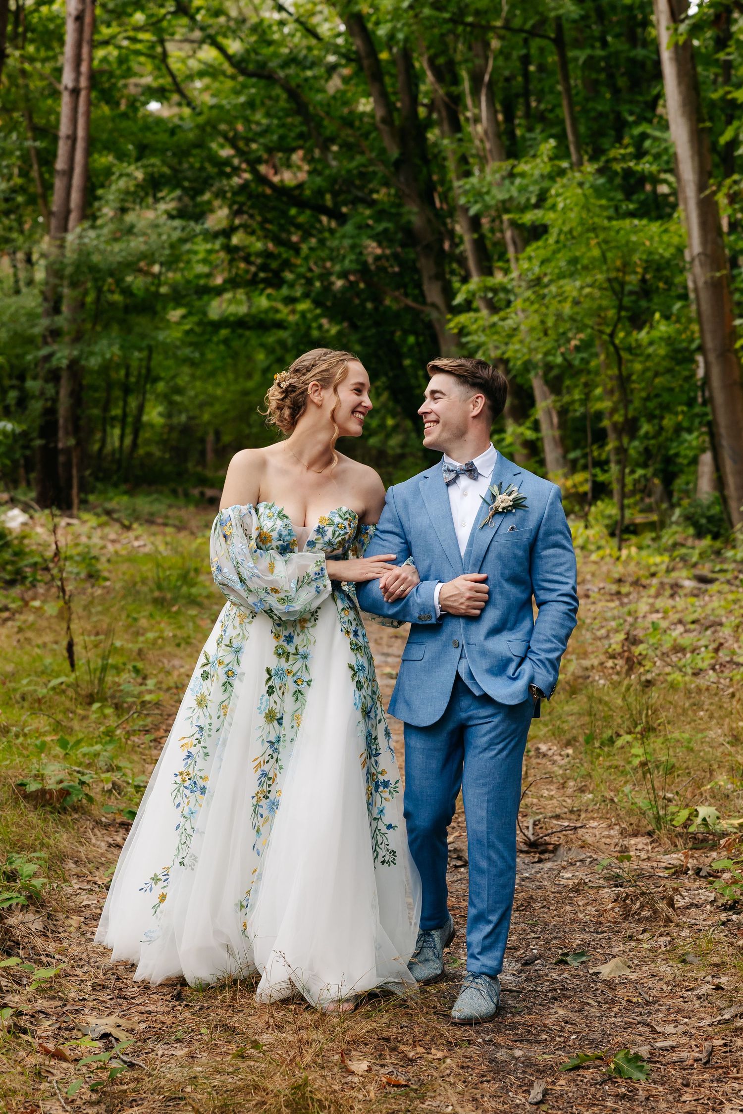 Happy bride and groom walking arm in arm through woodland path.