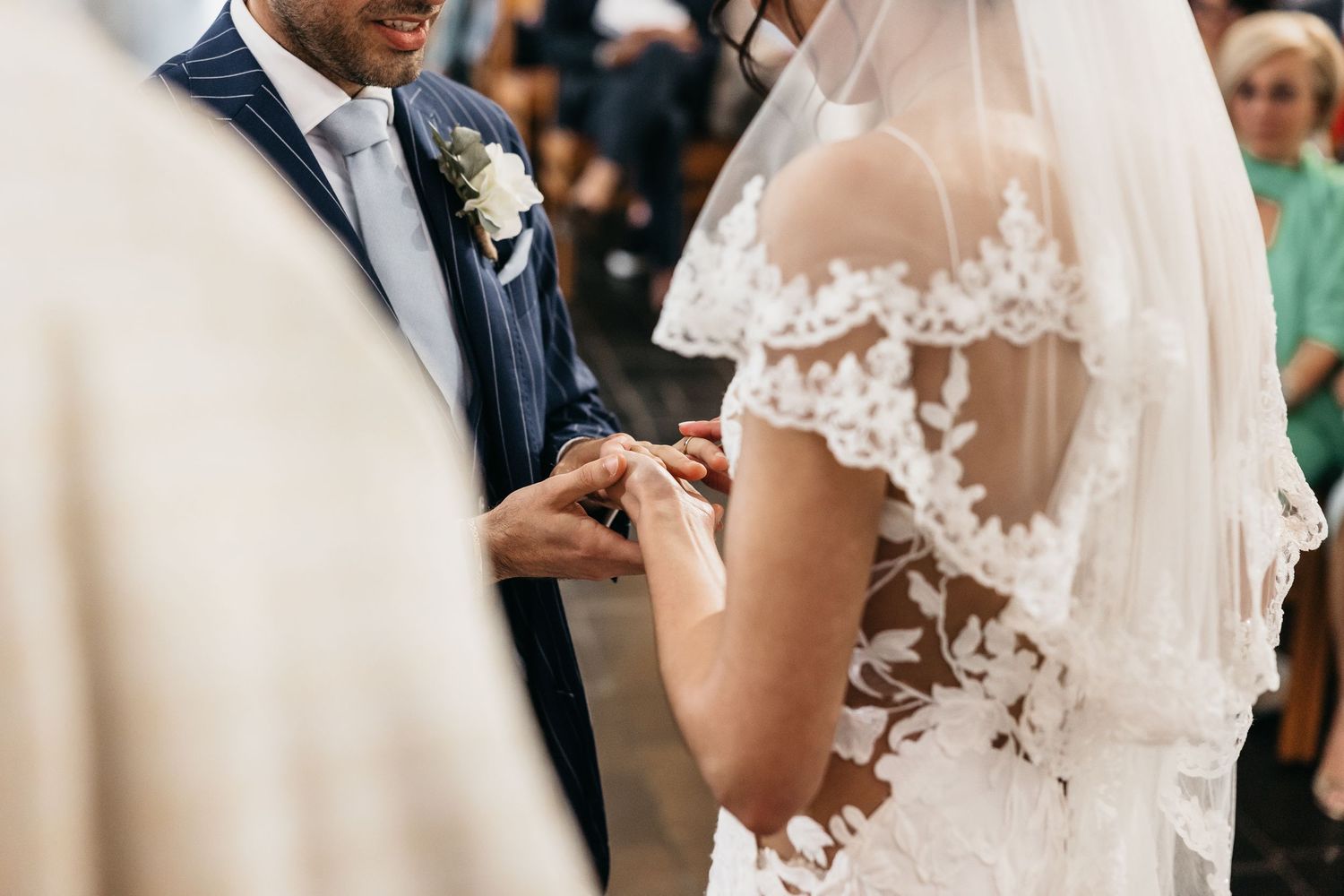 Groom placing wedding ring on brides finger while she wears lace veil during ceremony.