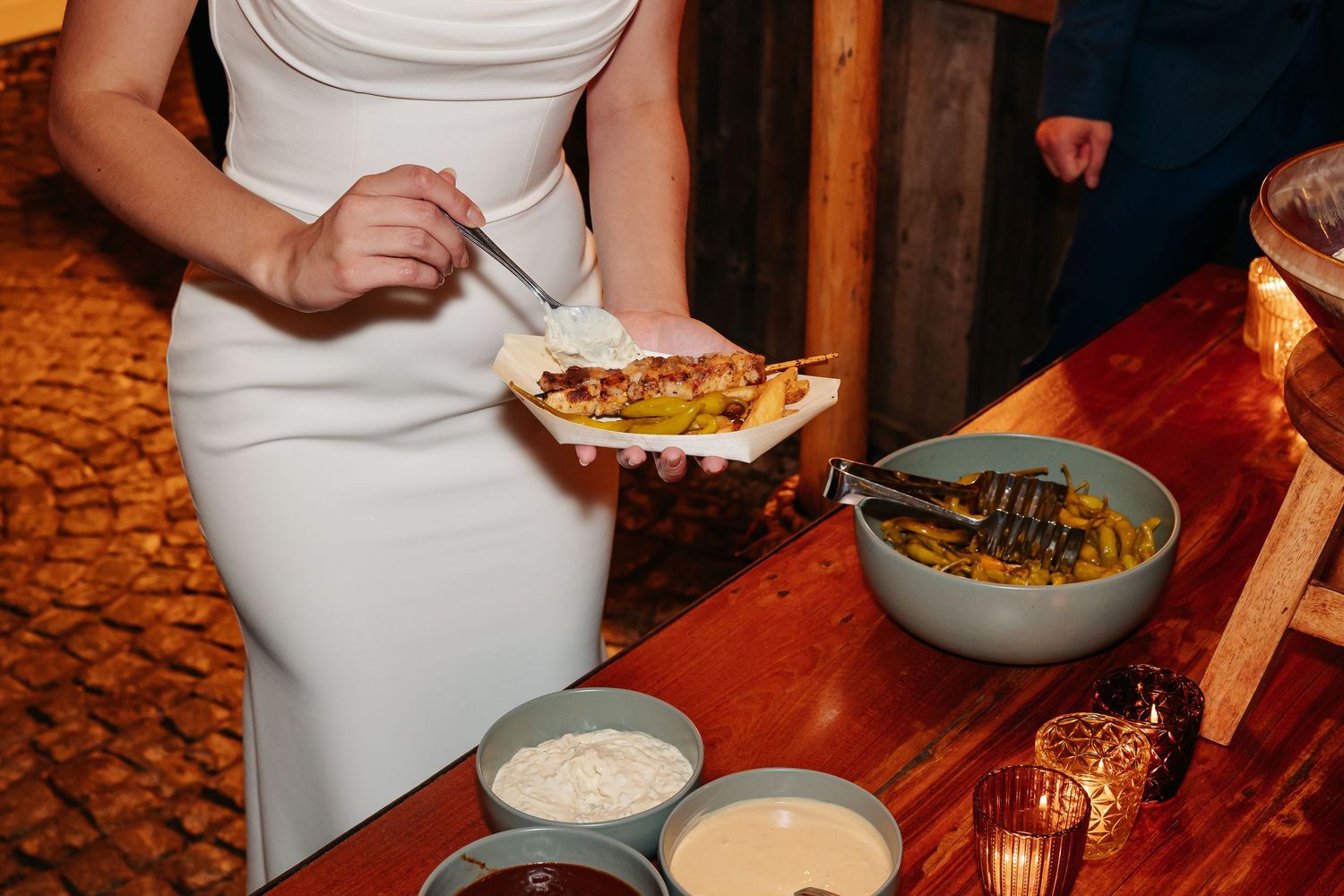 Bride in white dress serving herself food at a wedding reception buffet table.