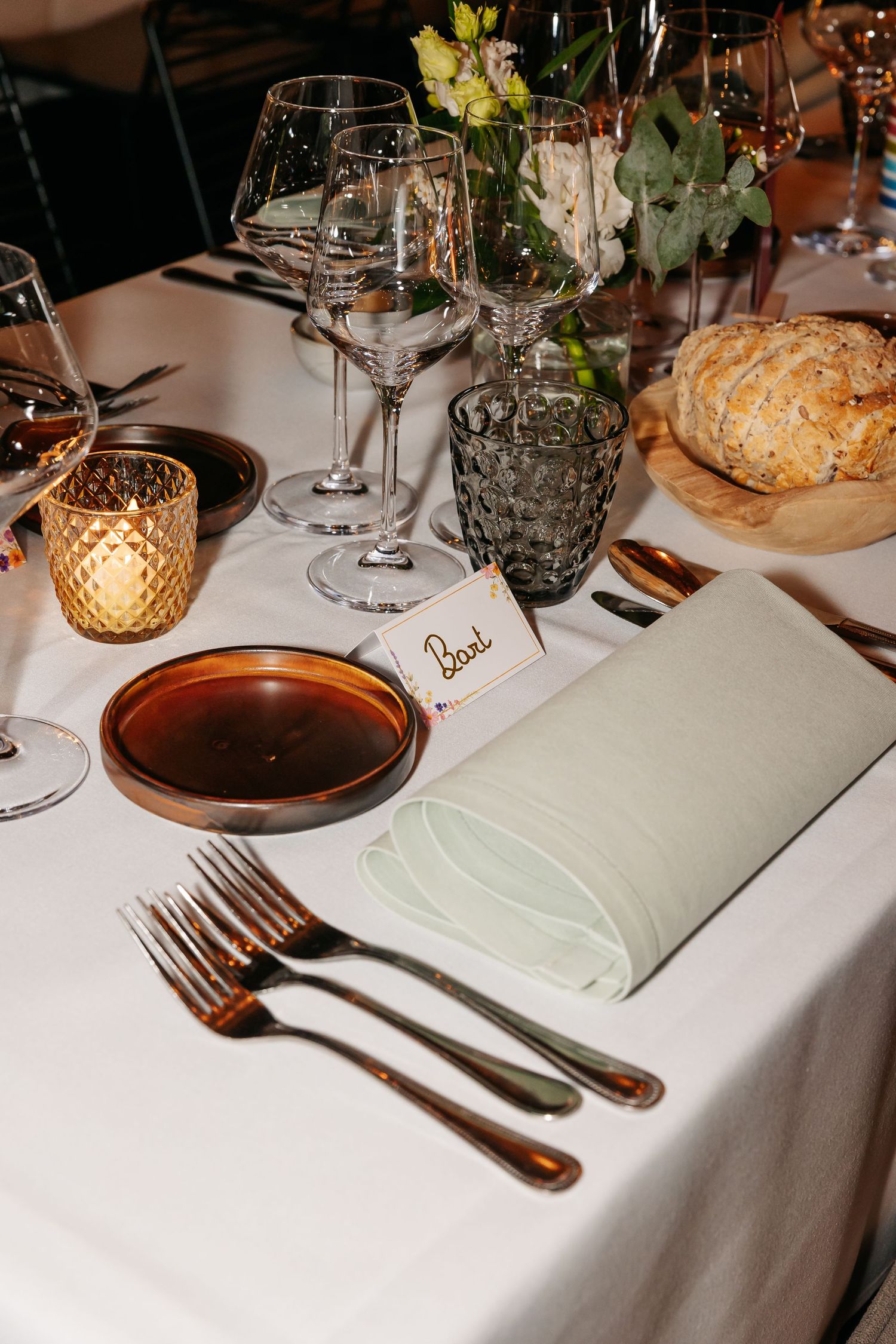 Elegant wedding table setting with bronze plates, crystal glasses, green napkin, candles, and a floral centerpiece.
