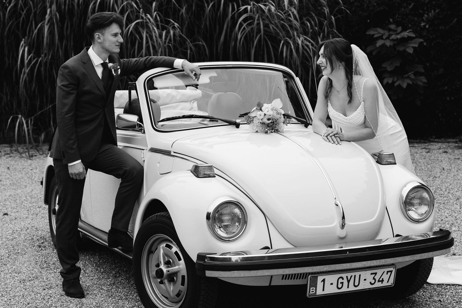 Black and white wedding portrait of bride and groom with a vintage VW Beetle convertible car.