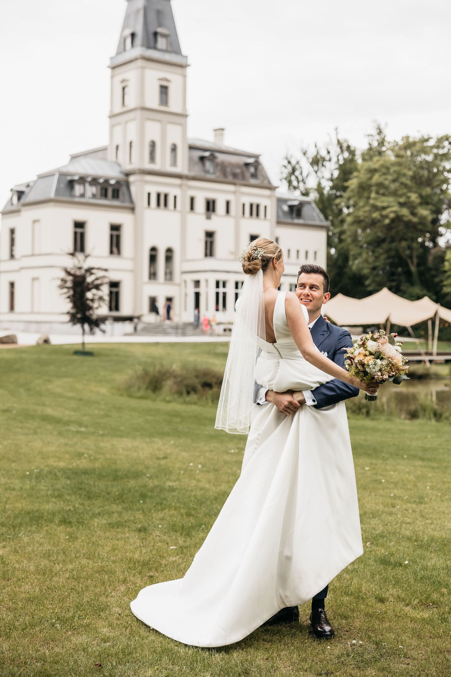 Groom lifting bride in a white gown on the lawn of a grand white chateau.