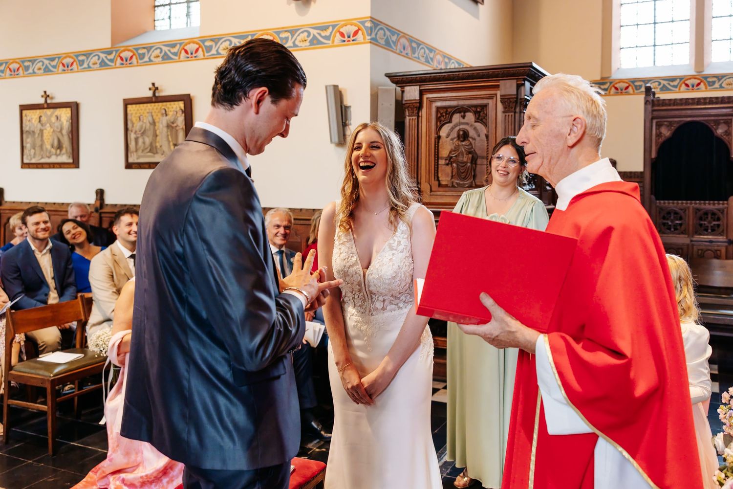 Bride and groom laughing joyfully with priest during church wedding ceremony.