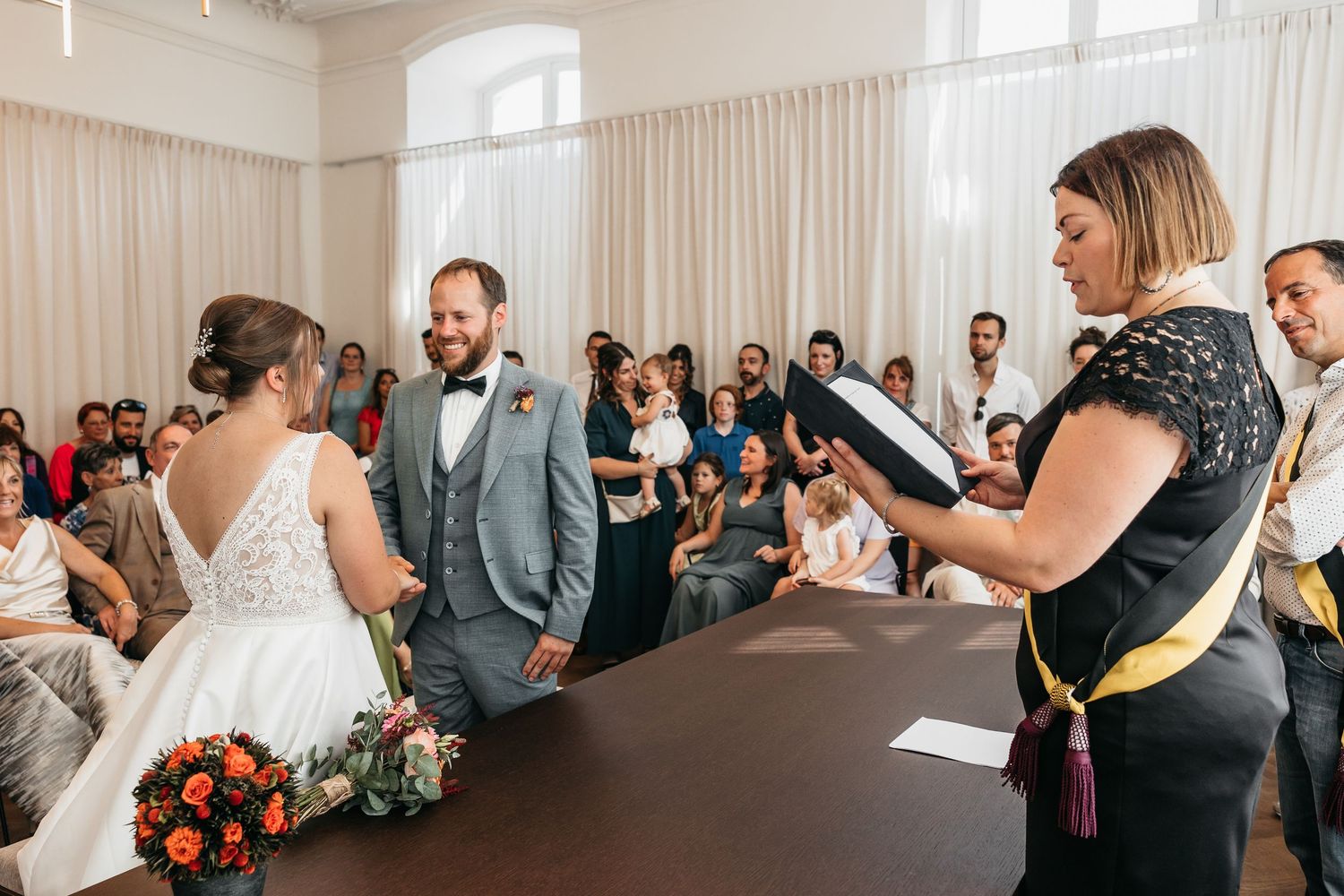 Wedding officiant reads vows to bride and groom during an intimate civil ceremony with seated guests.