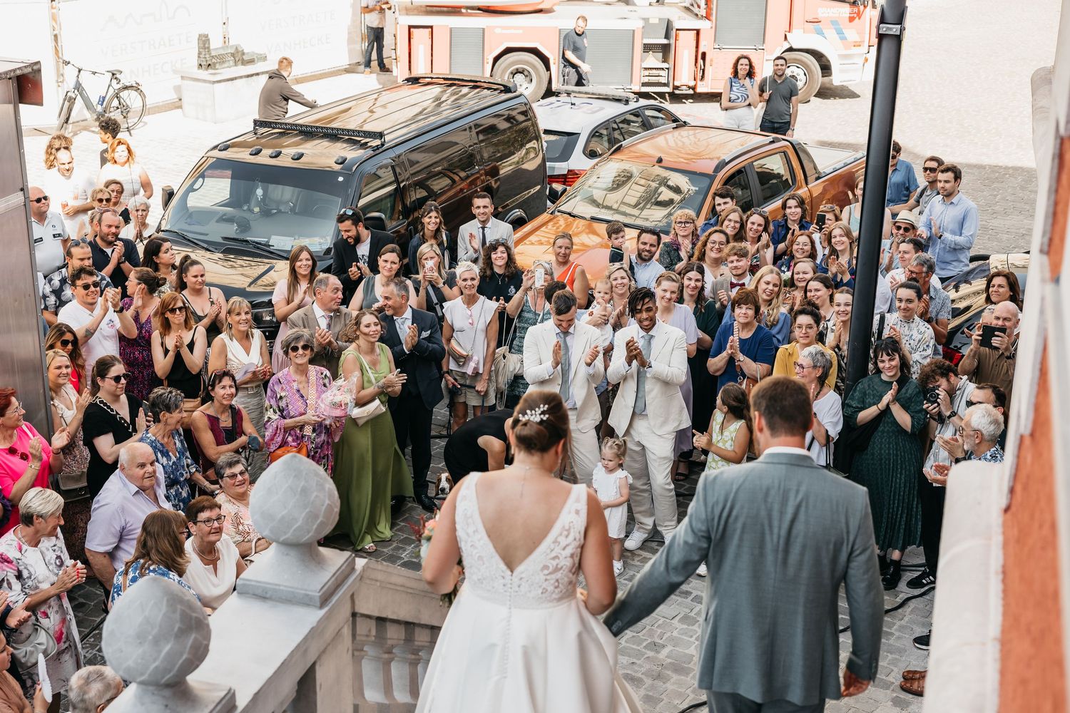 Bird's eye view of wedding guests applauding newlyweds descending outdoor steps after ceremony celebration.