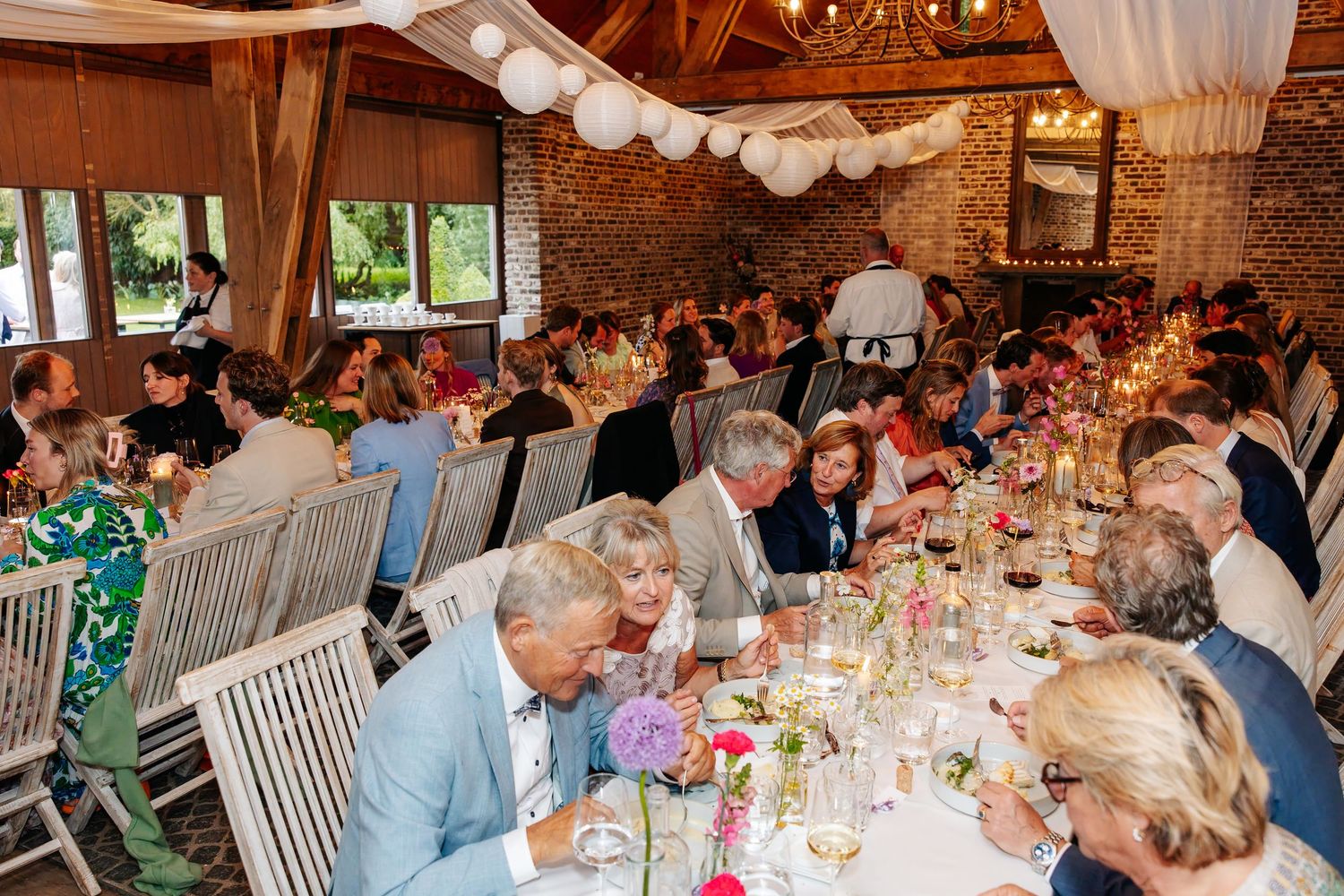 Large wedding reception dinner in a rustic barn venue with long tables and floral decor.