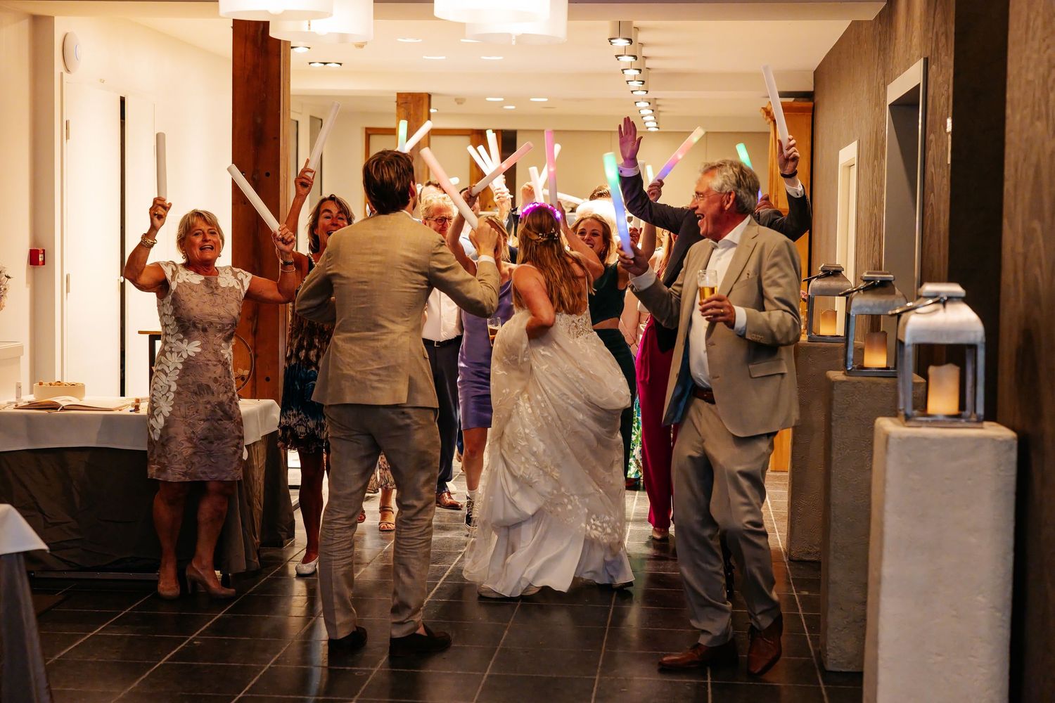 Bride and groom enter reception hall under raised sparklers held by cheering wedding guests.