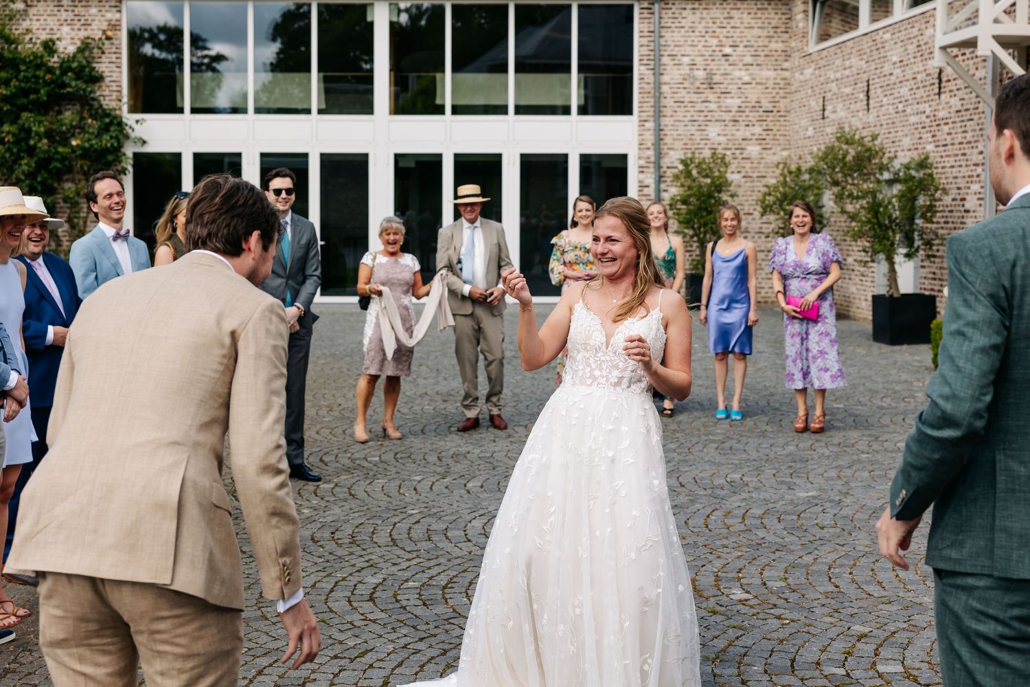 Bride in white gown using tin can telephone with wedding guests gathered outside.