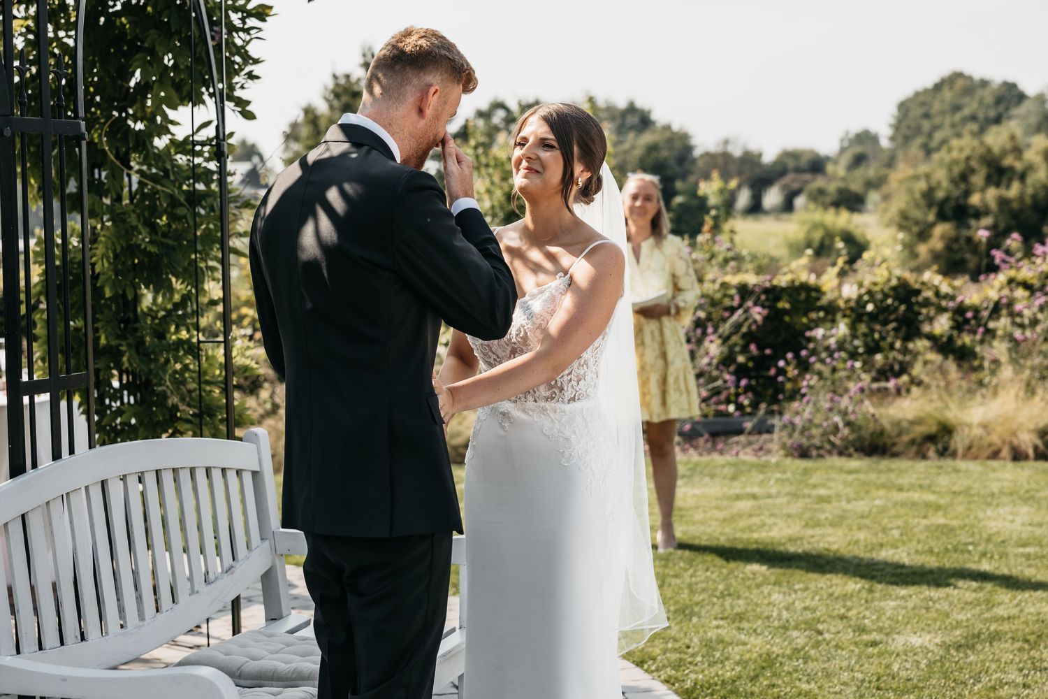 Groom wipes away tears during emotional first look moment with bride in garden setting.