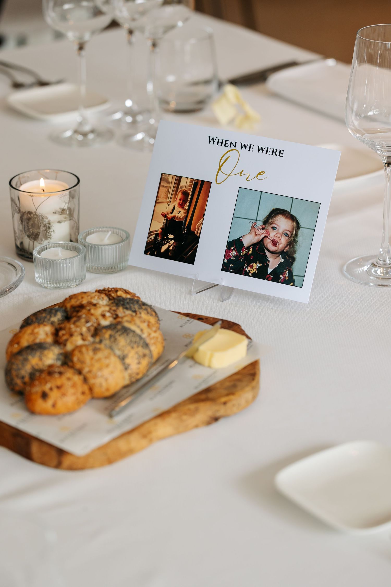 Wedding table centerpiece featuring a bread board, butter, candles, and a childhood photo display card.