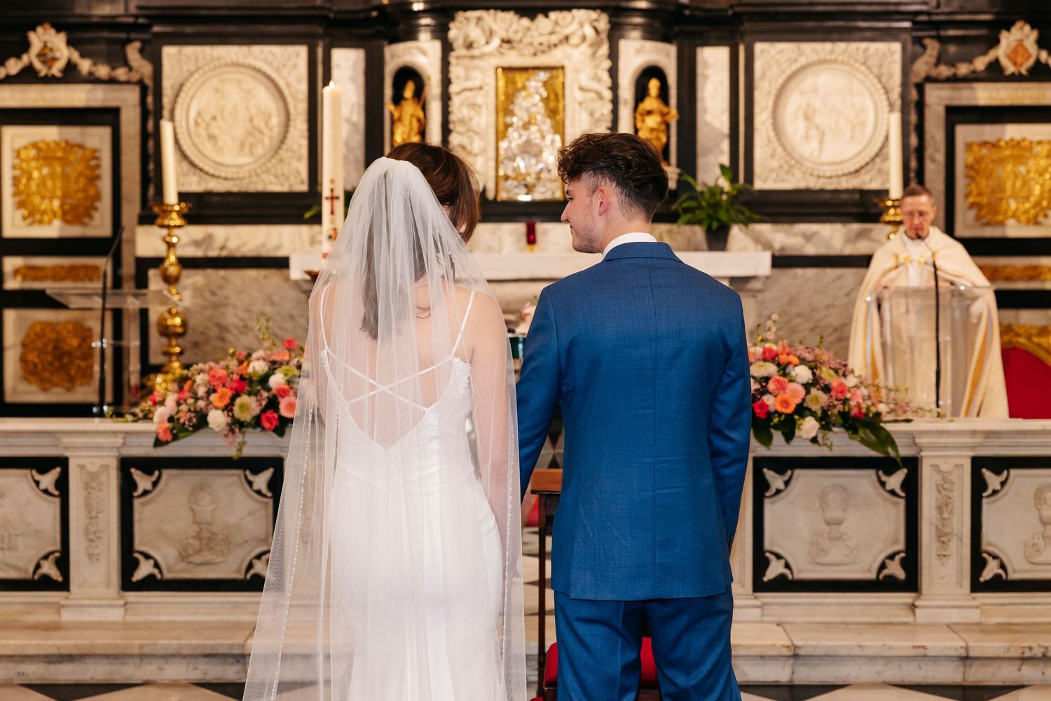 Bride and groom stand before ornate church altar during Catholic wedding ceremony.