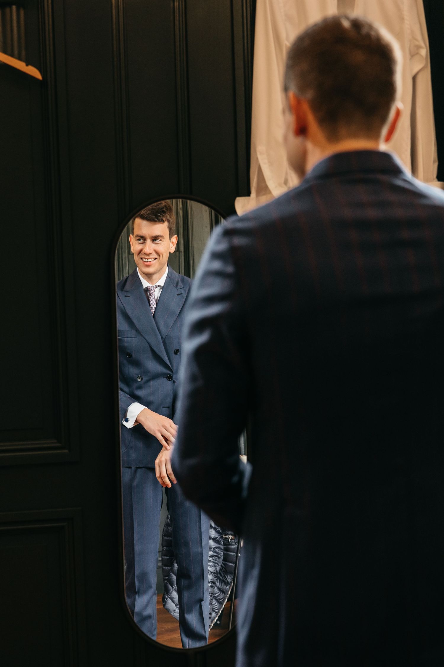 Handsome groom in navy plaid suit smiling at his reflection in an oval mirror.