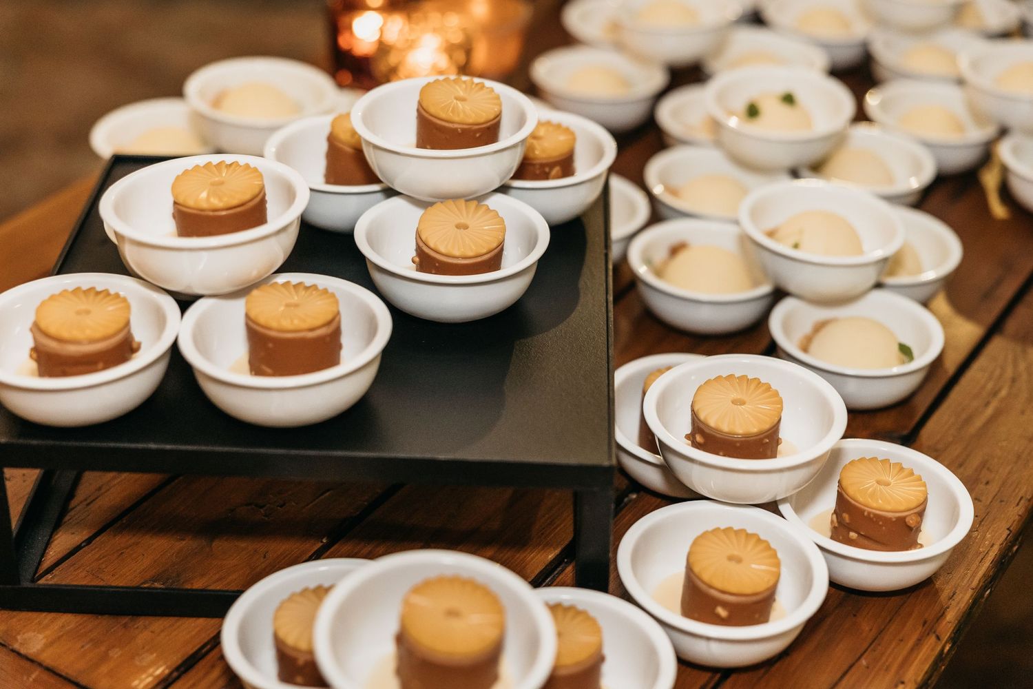 Rows of individual caramel desserts in white ceramic bowls arranged on wooden display at wedding reception.