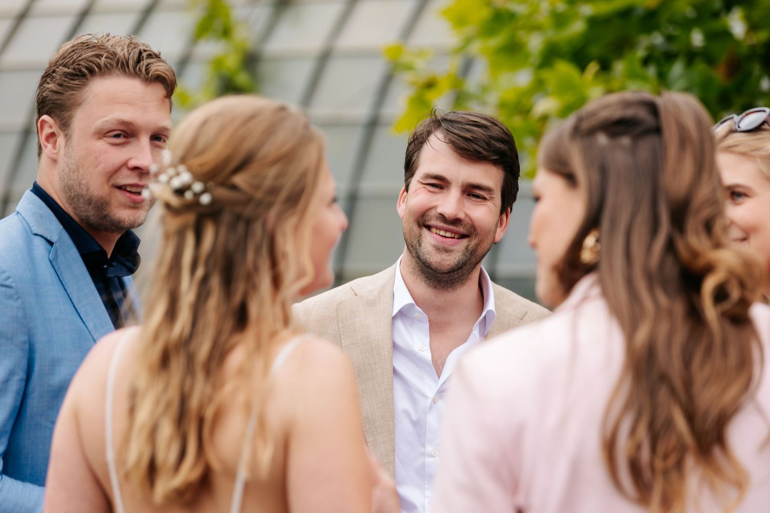 Three wedding guests smiling and conversing outdoors, men in blue and beige suits at summer celebration.